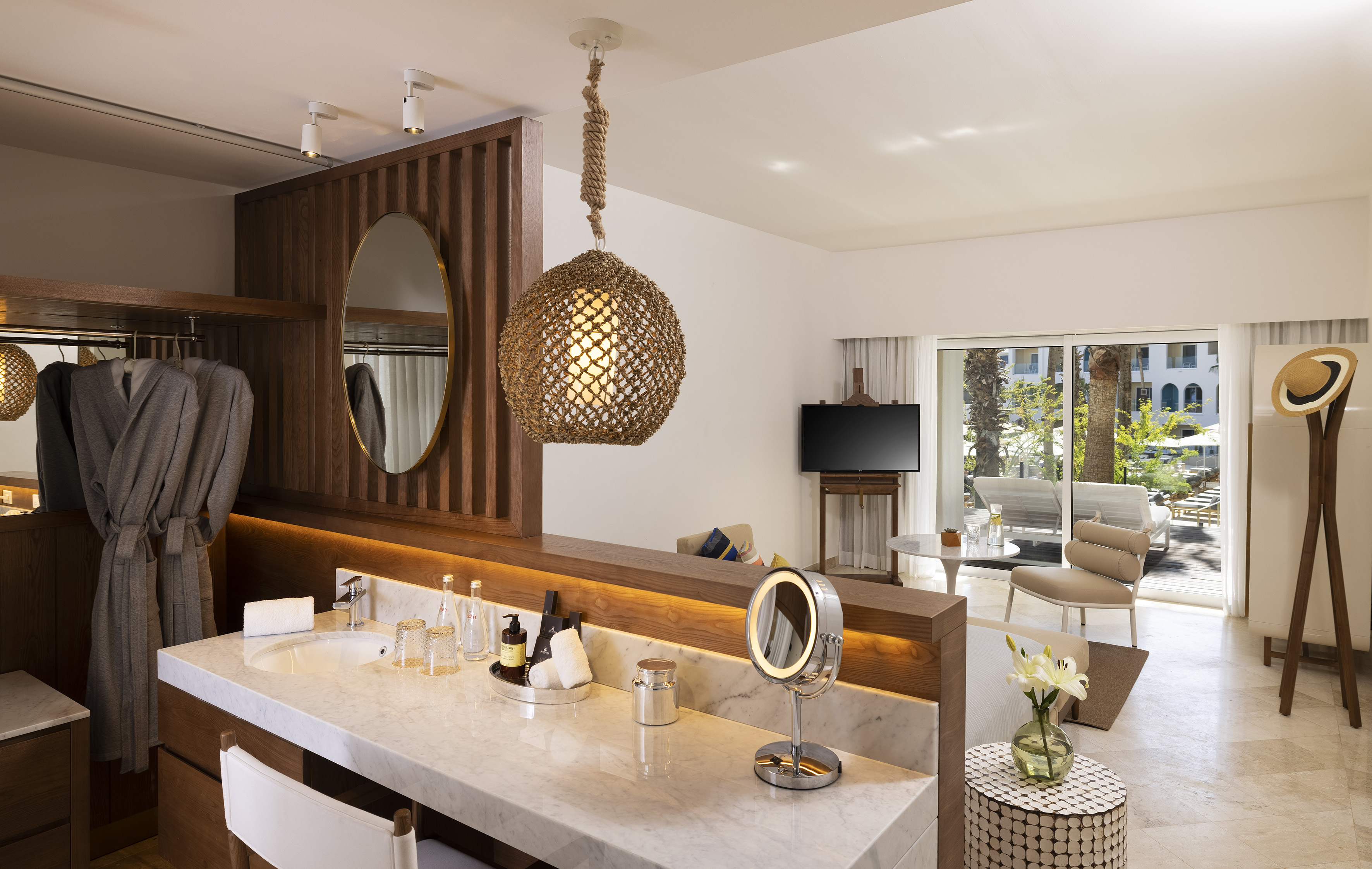 Luxury hotel room with marble vanity, living area, and tropical resort view.