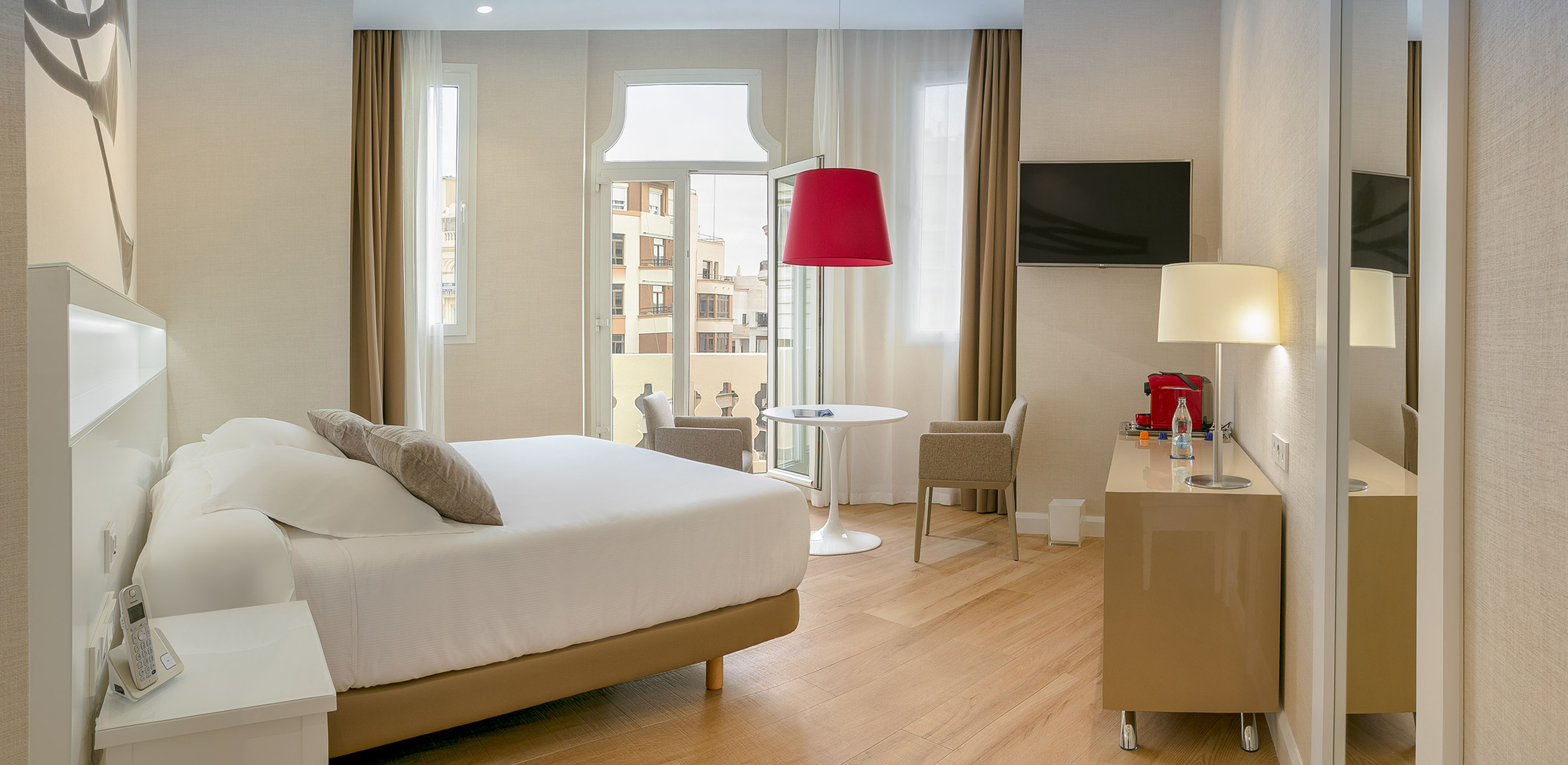 Modern hotel room with white bed, wood floor, red pendant lamp, balcony city view.