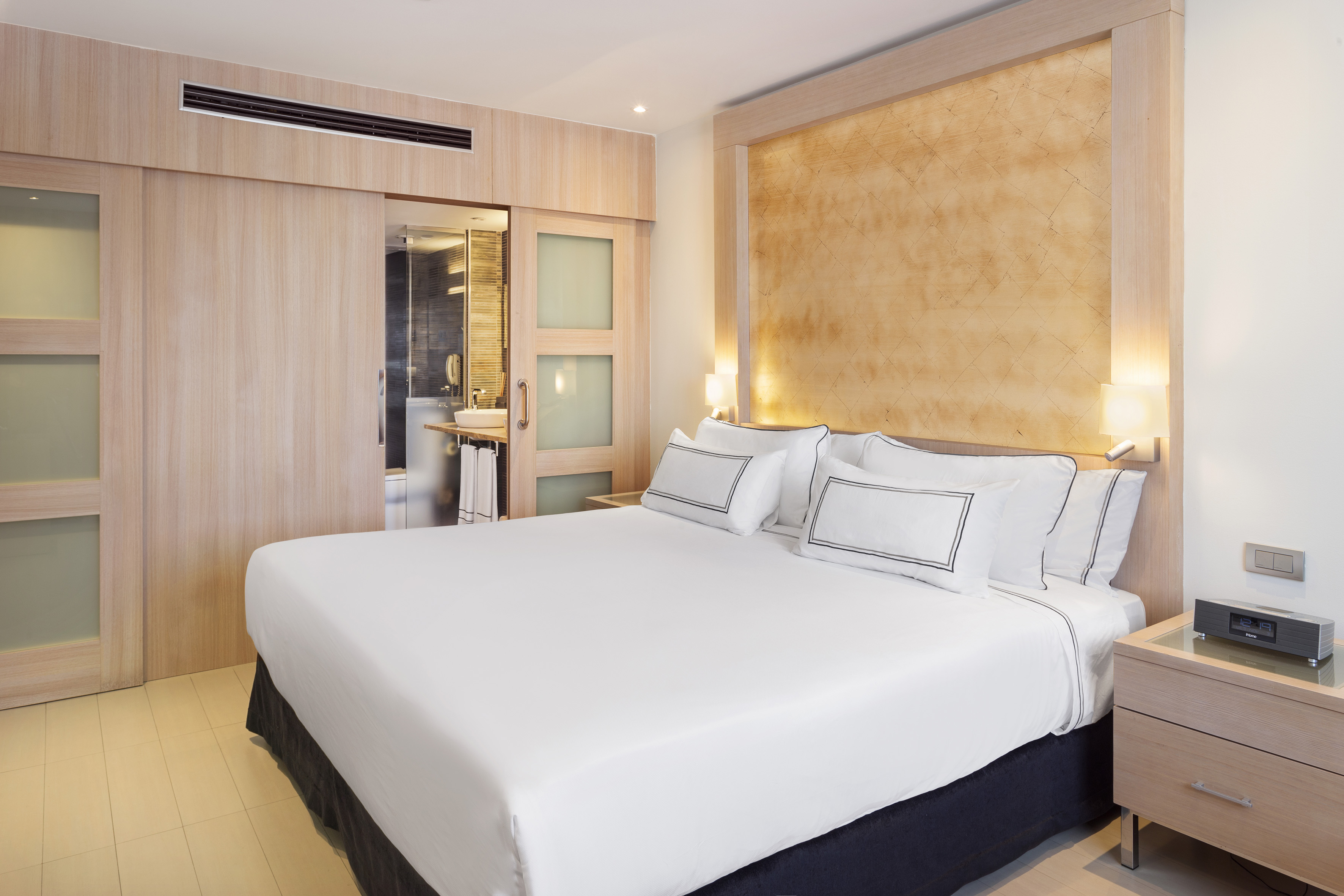 Contemporary hotel room with white bed, wooden panels, and ensuite bathroom.