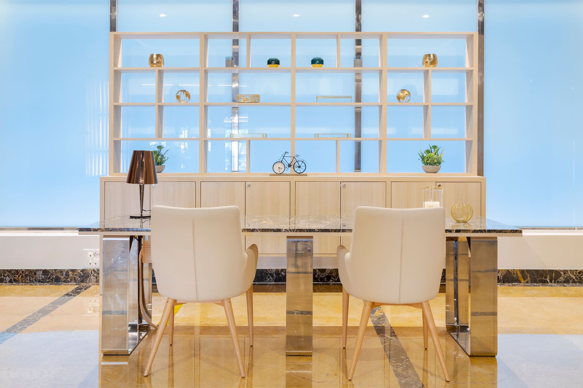 Modern lobby seating with cream chairs, marble table, wooden shelving.