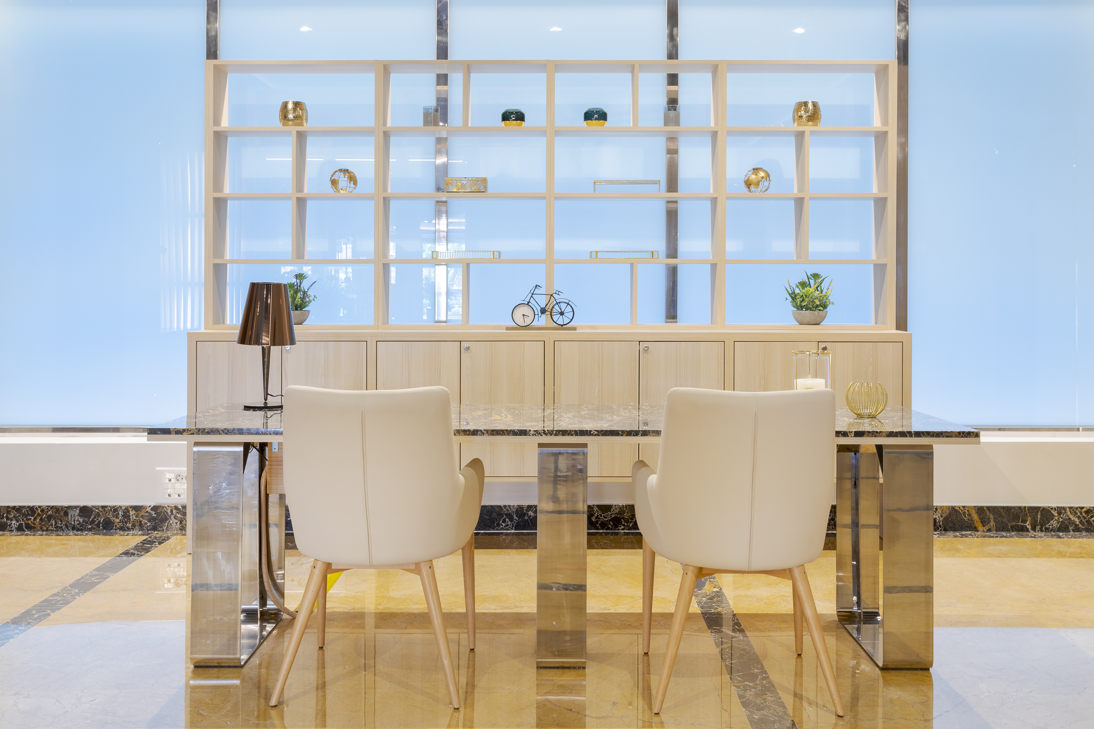 Modern lobby seating with cream chairs, marble table, wooden shelving.