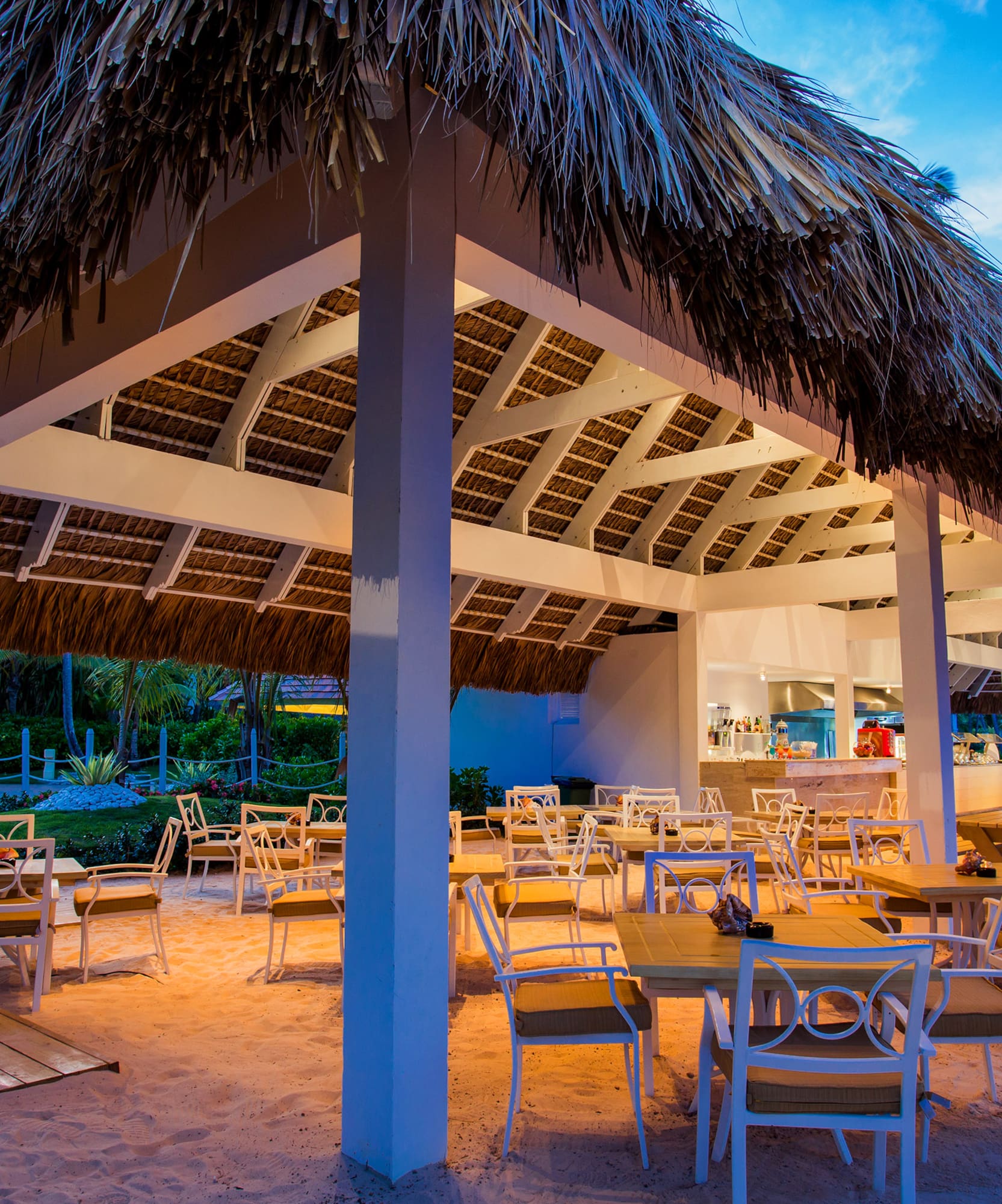 a restaurant with tables and chairs under a thatched roof