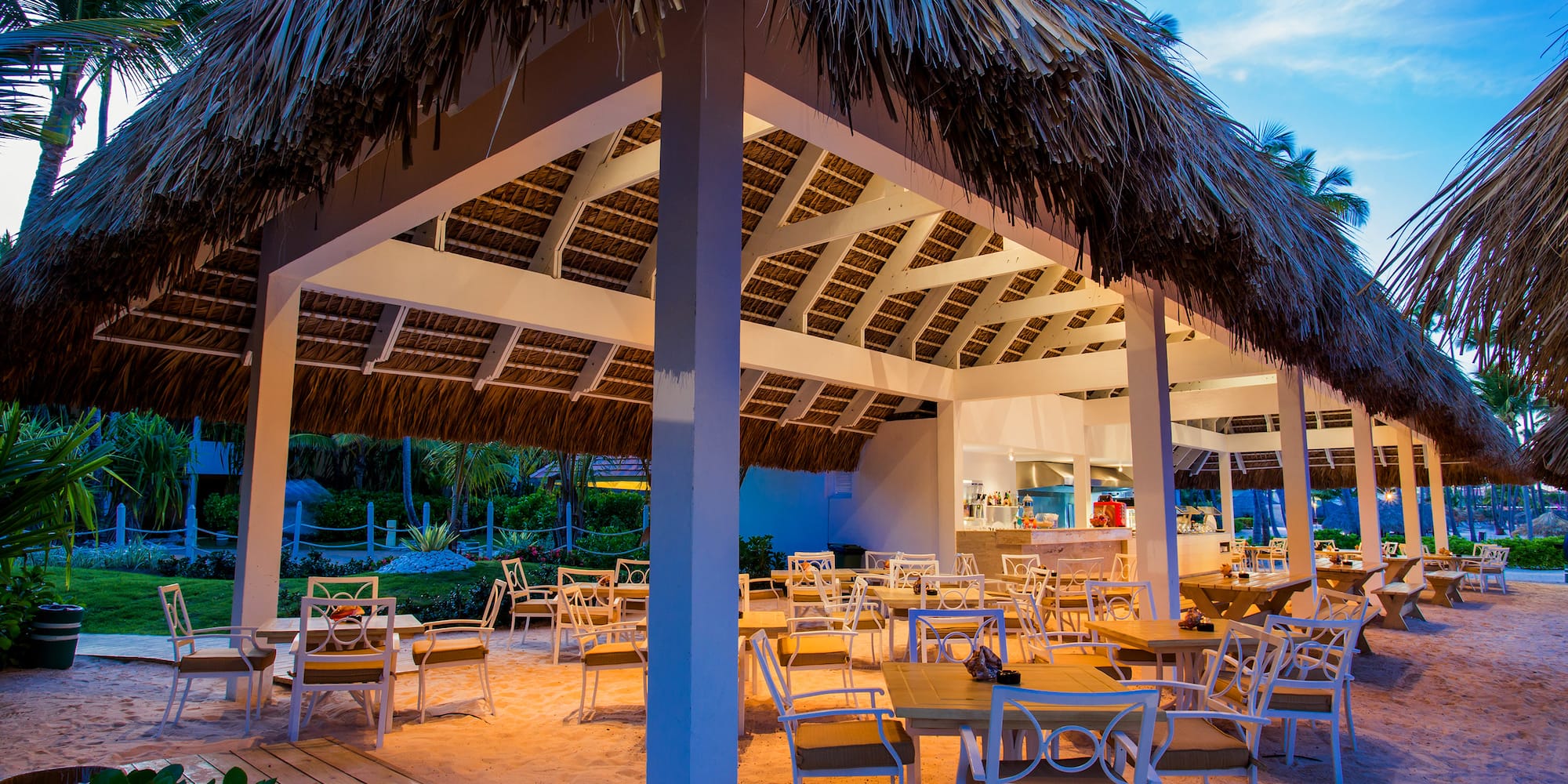 a restaurant with tables and chairs under a thatched roof