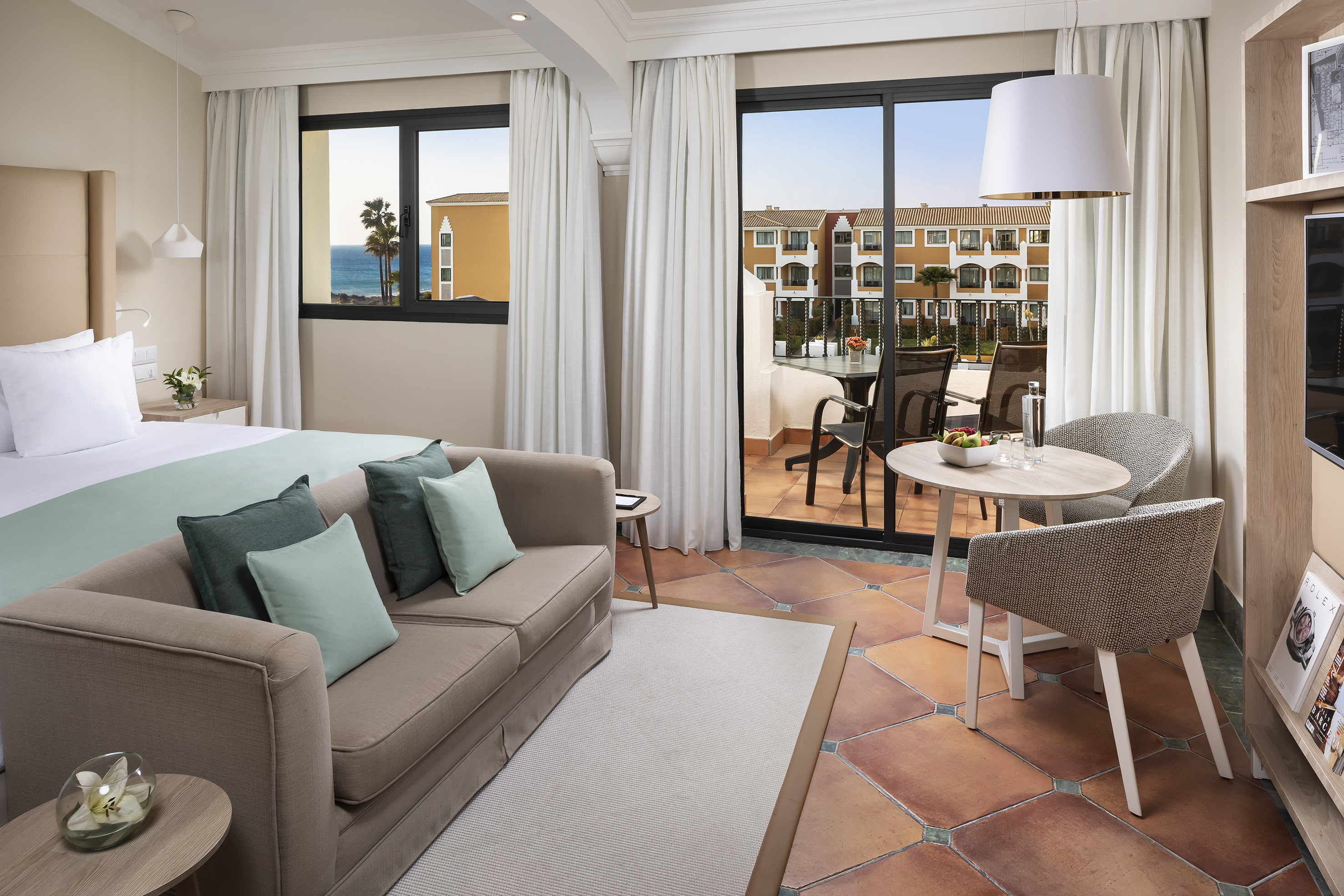 Modern resort suite with sea view, balcony, sofa, and comfortable bed.