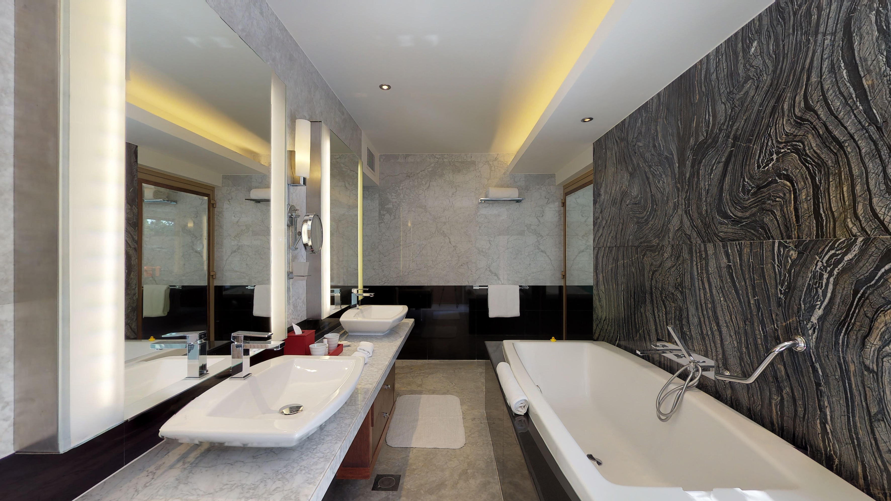 Luxury hotel bathroom with dual vessel sinks, large tub, and striated dark stone.