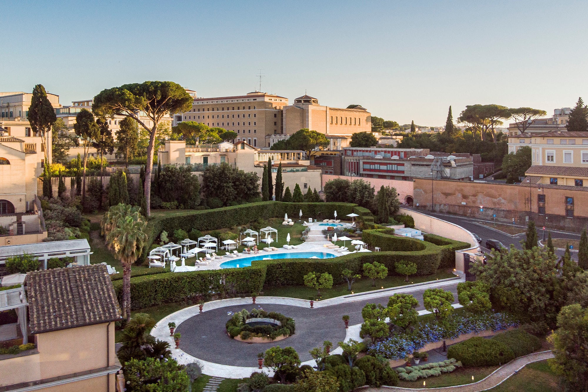 Aerial view of luxurious hotel pool, manicured gardens, and city buildings.