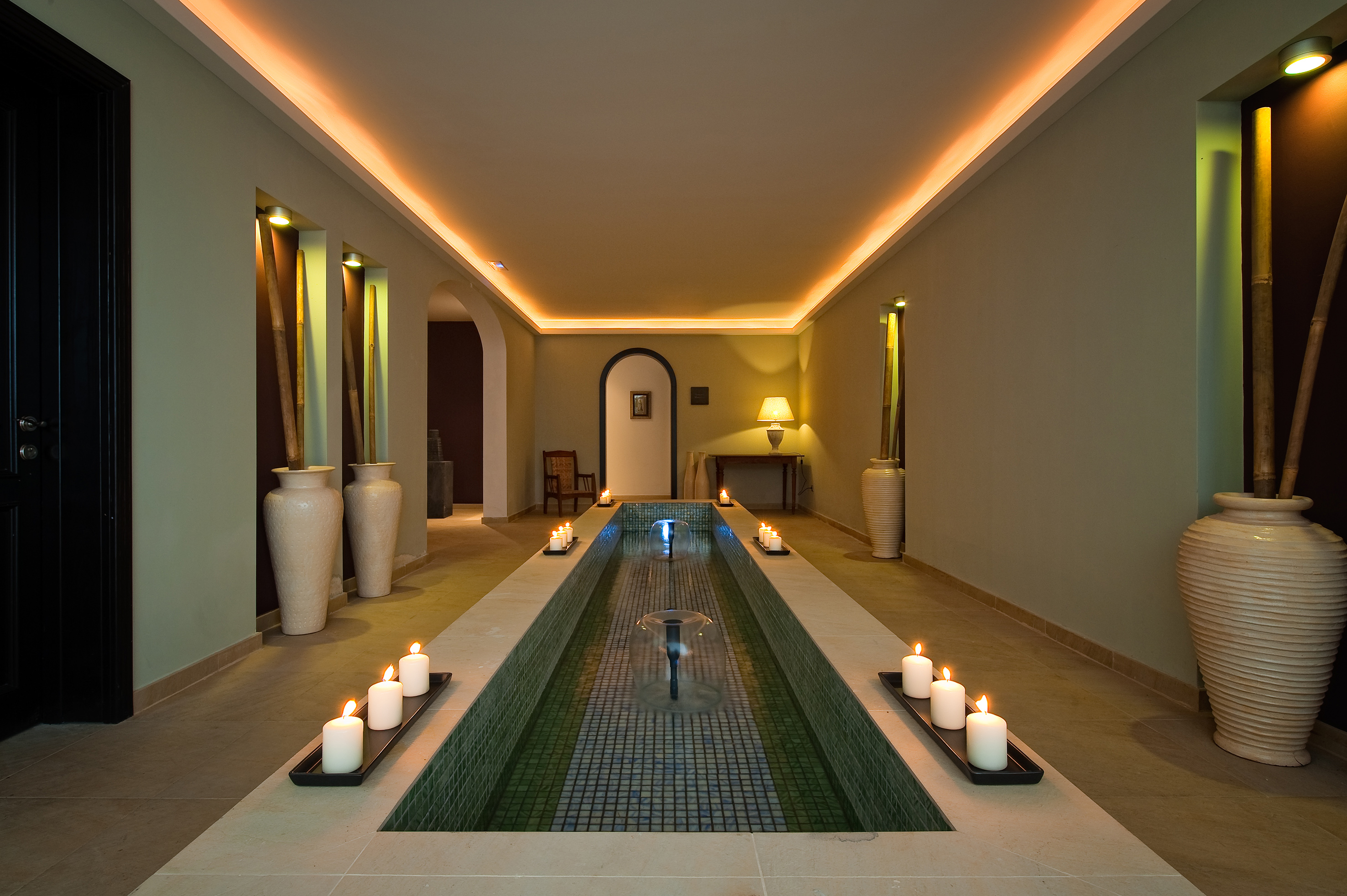 Spa corridor with candlelit water fountain, warm ambient lighting, and bamboo decor.