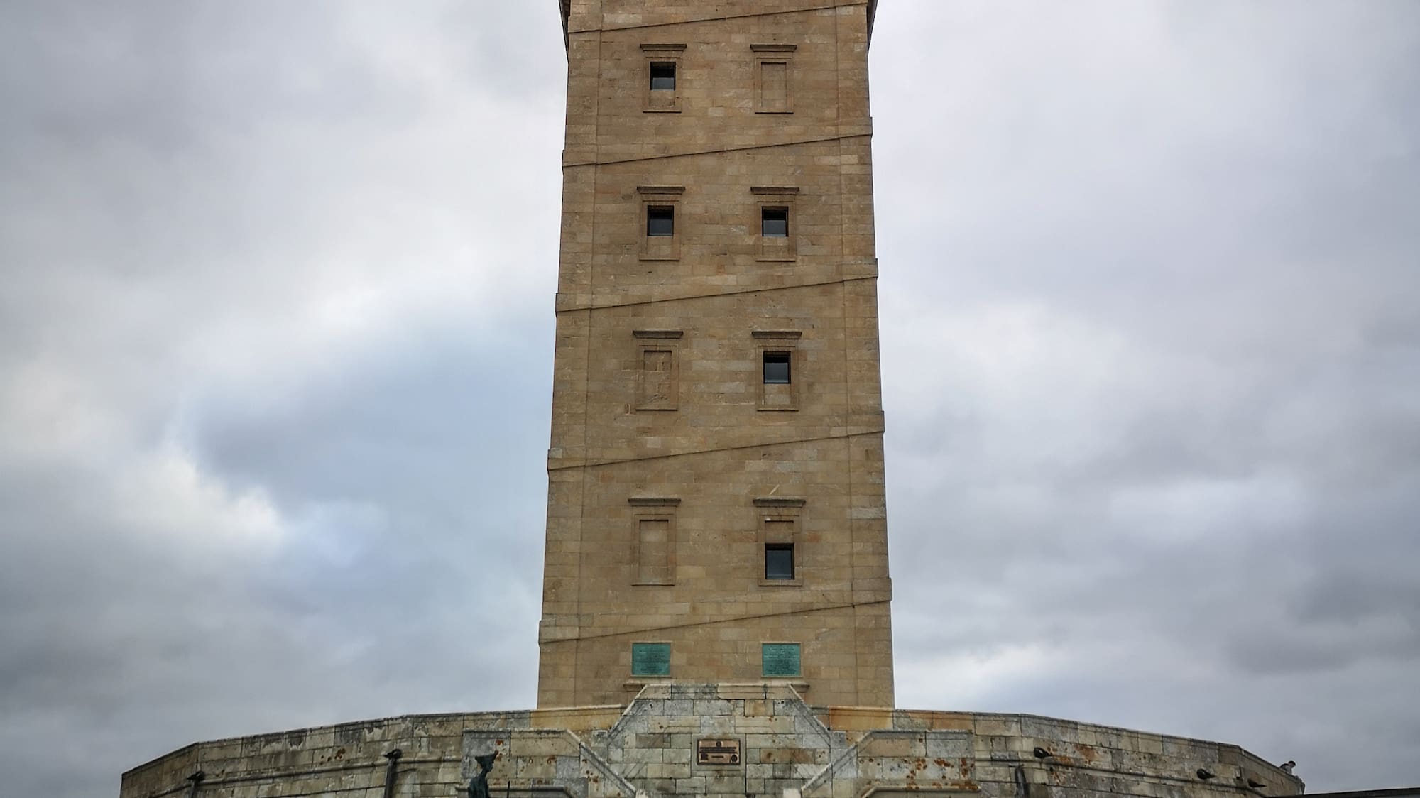 a tall tower with a steeple with Tower of Hercules in the background