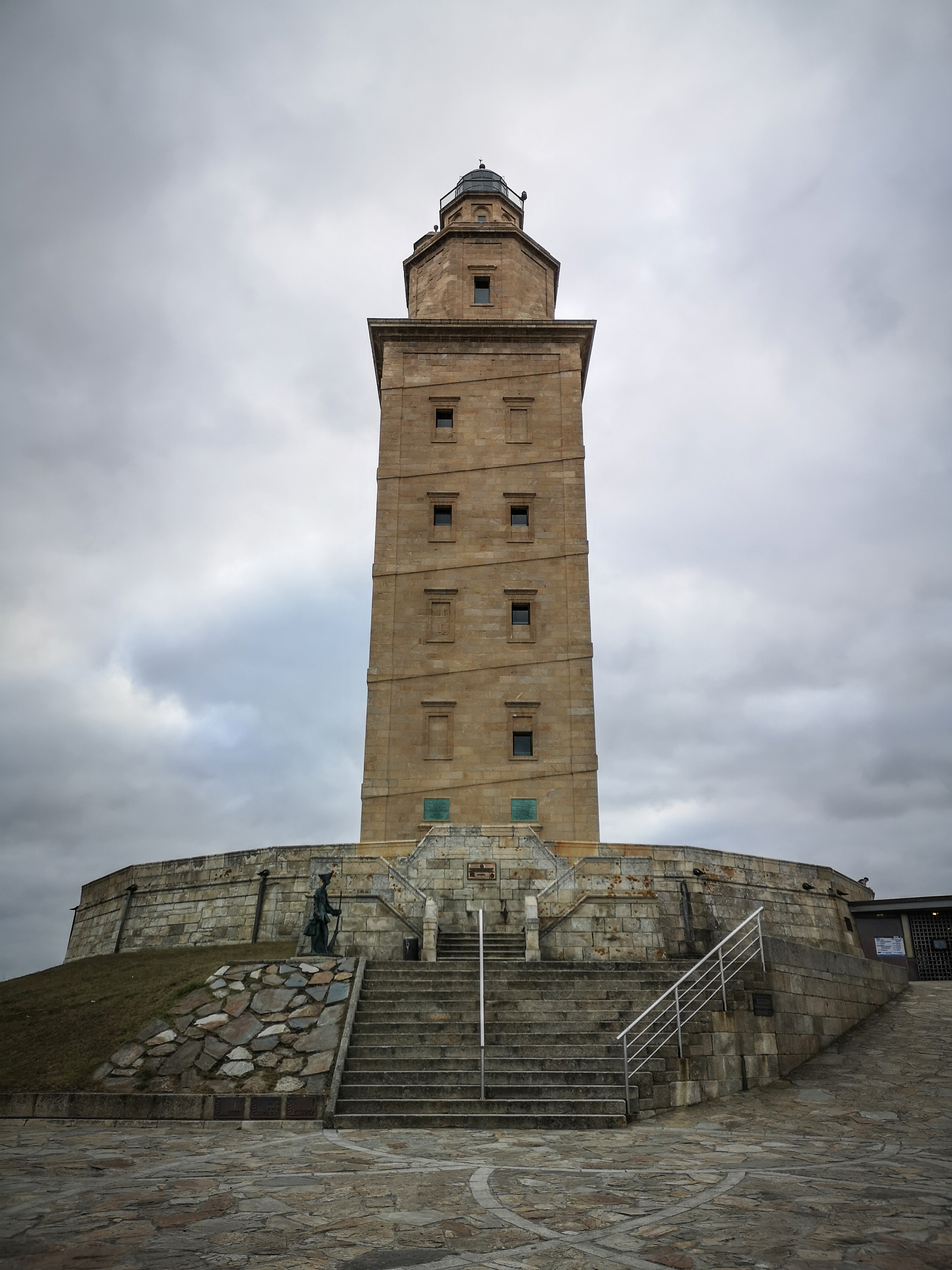 a tall tower with a steeple with Tower of Hercules in the background