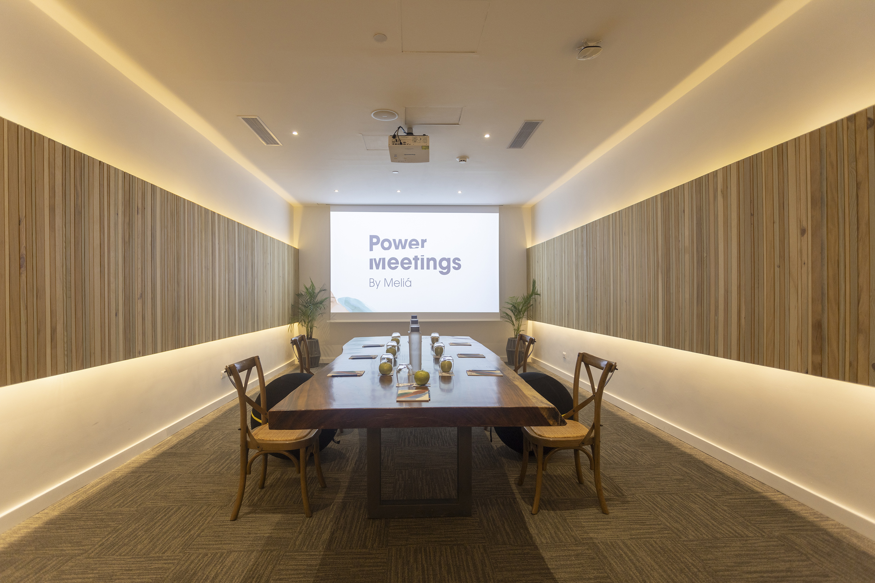 Modern meeting room with wooden table, 'Power meetings' on projector screen.