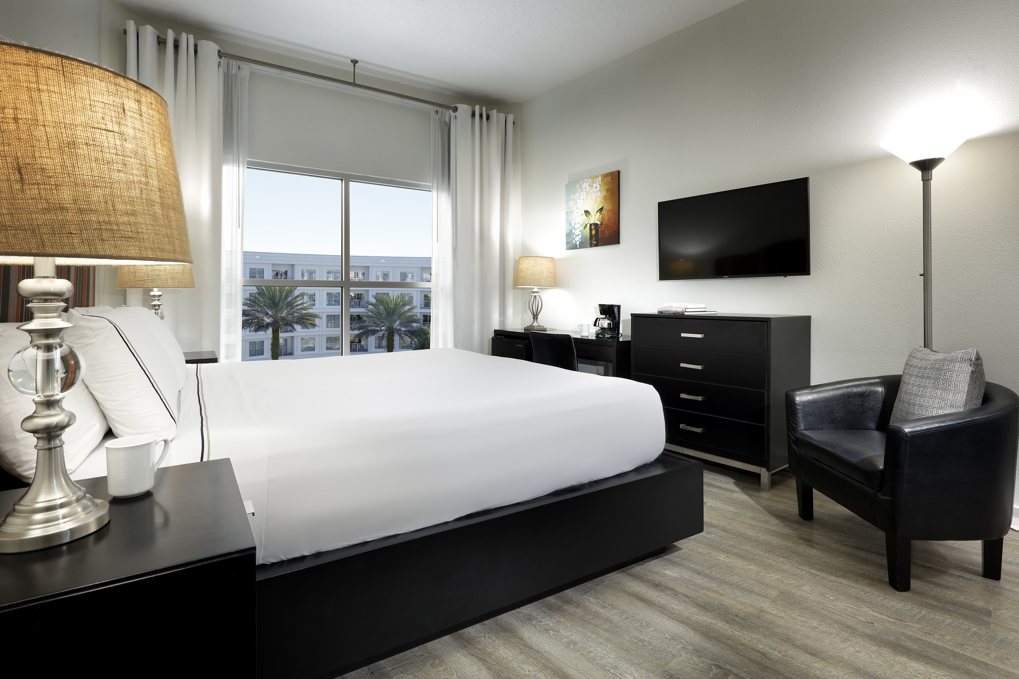 Modern hotel room with white bed, TV, desk, armchair, and window with palm view. - Meliá Room - Meliá Orlando Celebration, Orlando