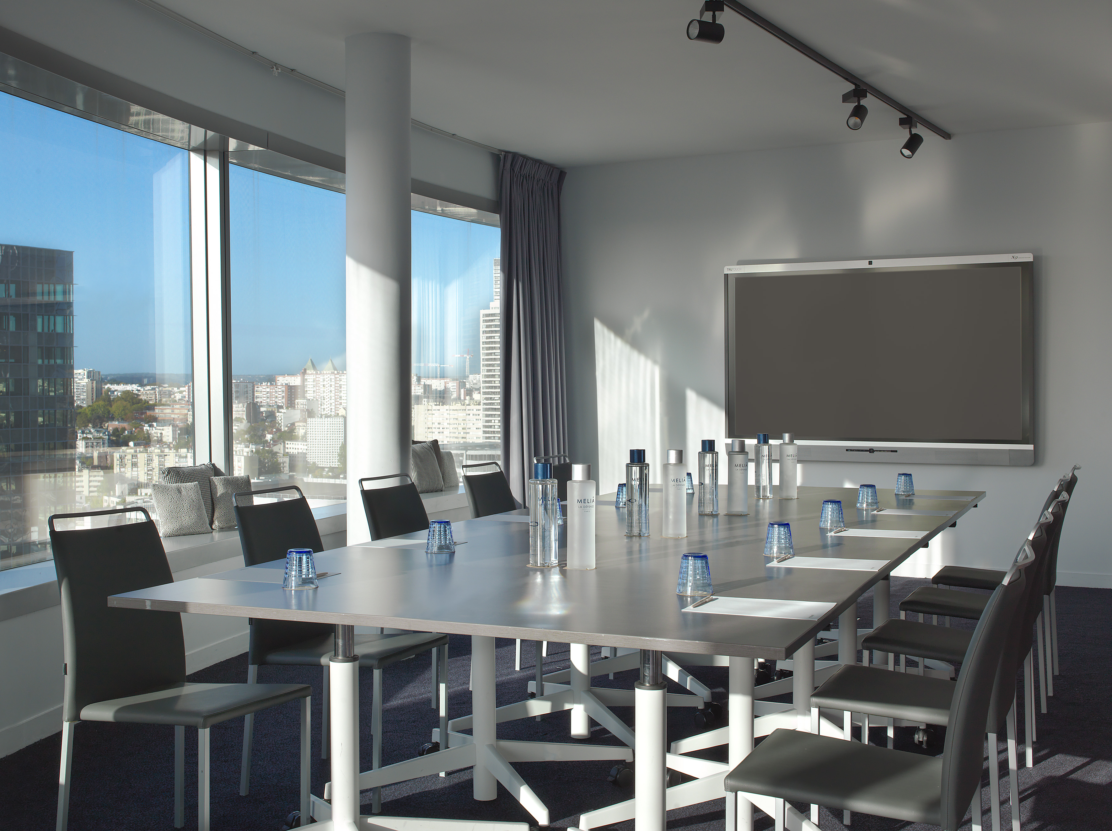 Modern meeting room with city view, long conference table, and digital screen.