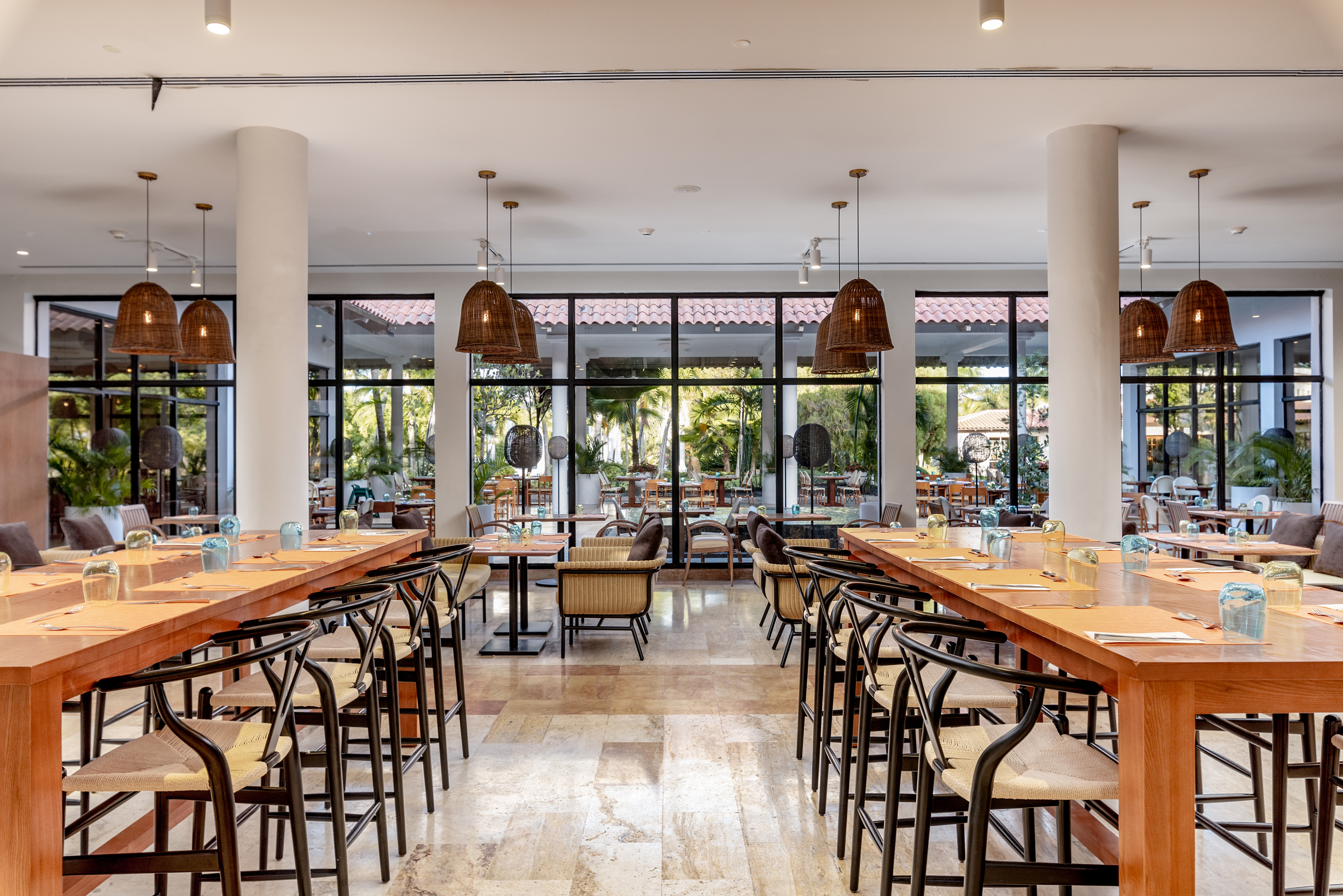 Tropical restaurant with wooden tables, wicker lights, and outdoor garden views.