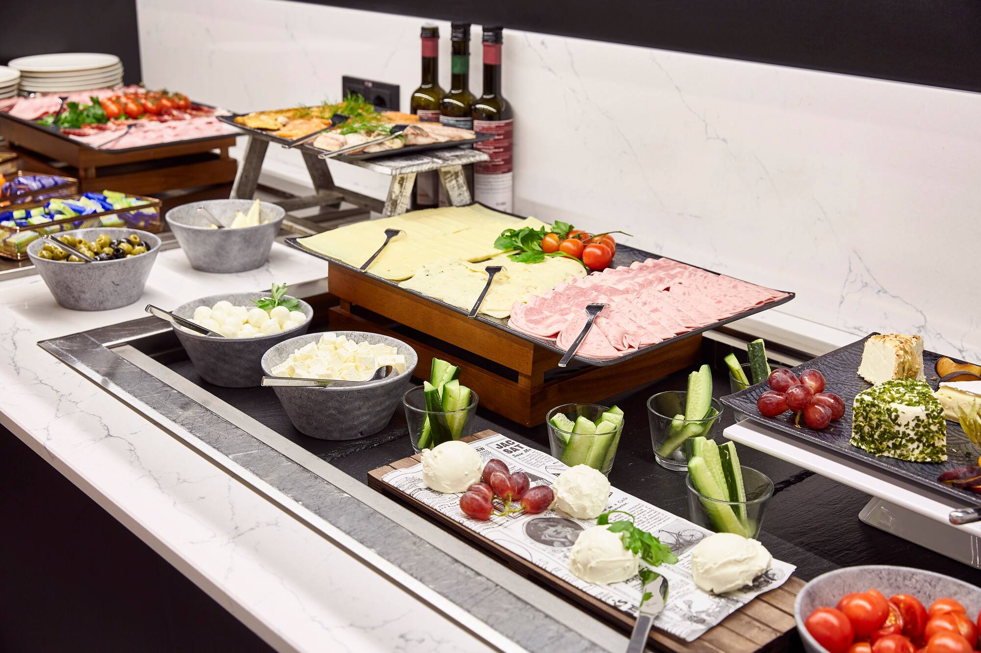 Breakfast buffet with cheeses, deli meats, olives, and fresh produce.