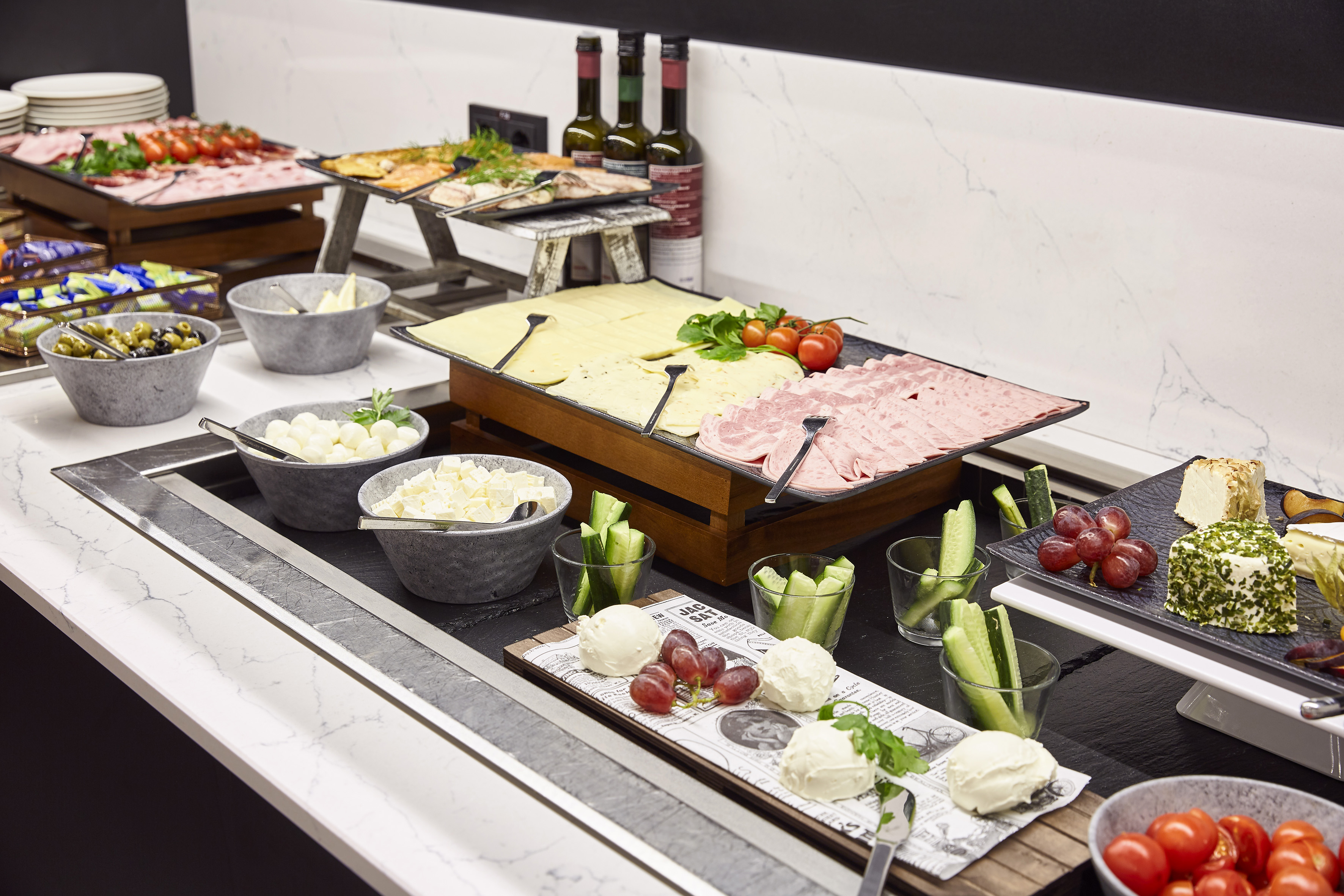 Breakfast buffet with cheeses, deli meats, olives, and fresh produce.