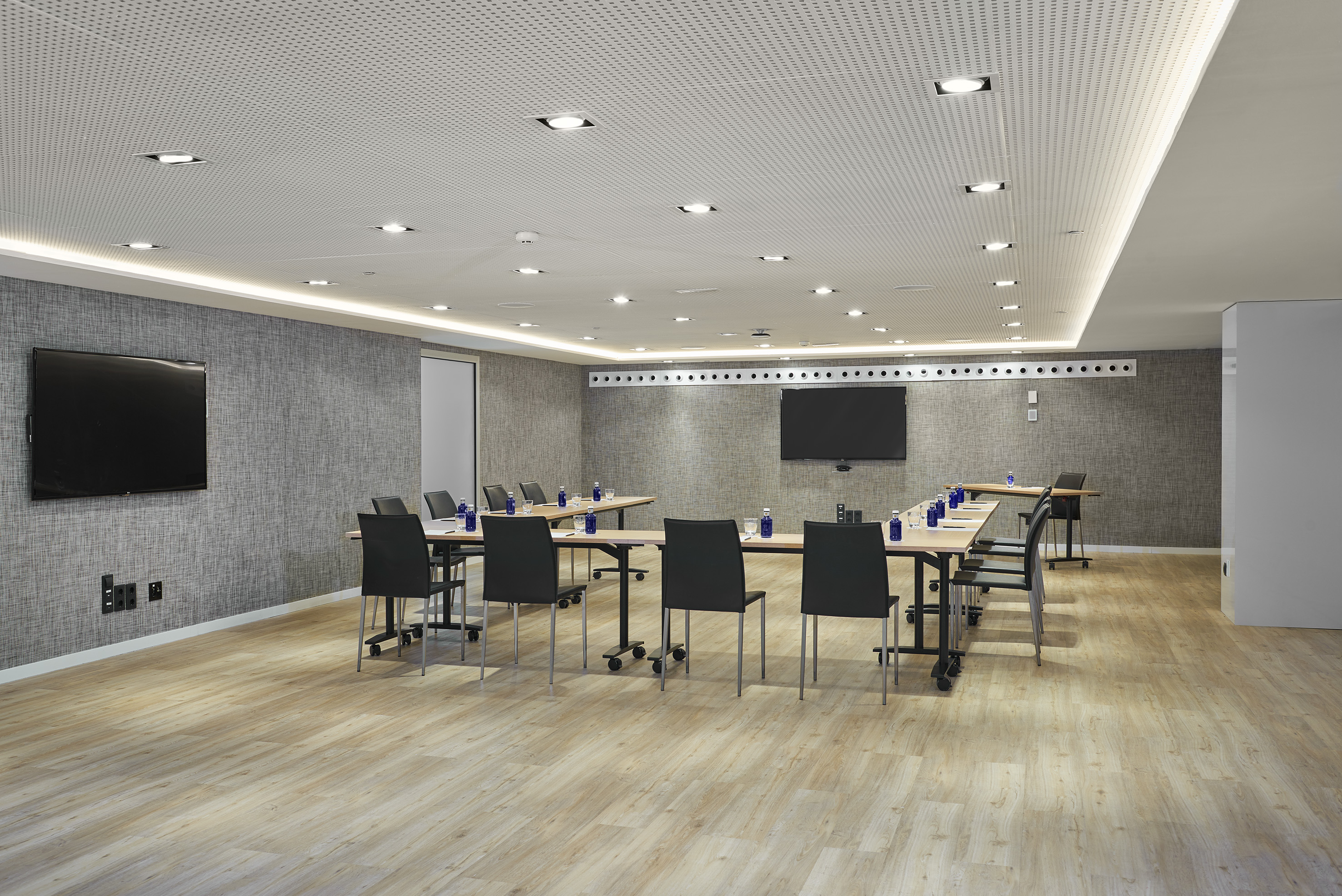 Modern conference room with U-shaped tables, dual screens, and wooden floor.