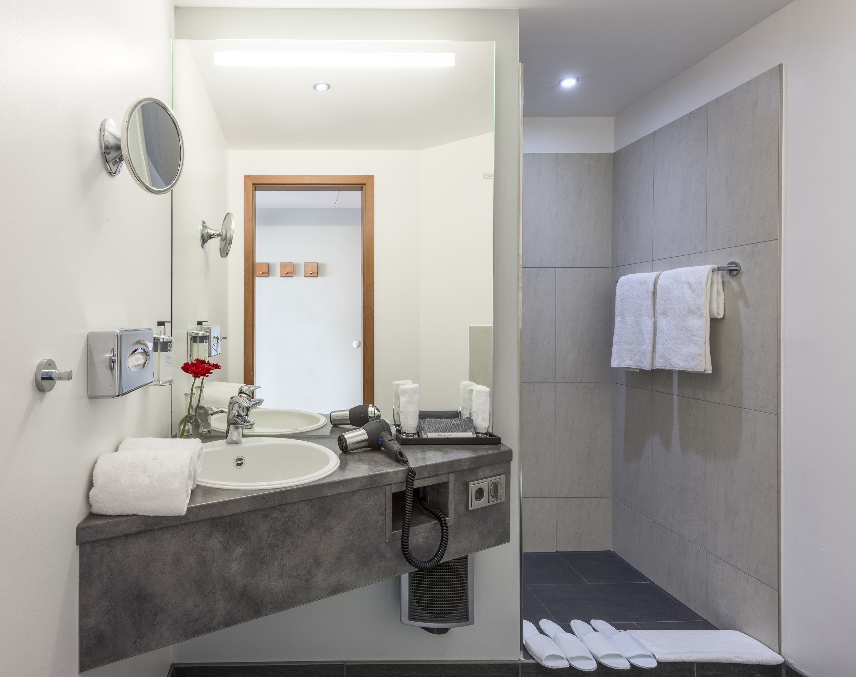 Modern hotel bathroom with vanity, sink, mirror, shower, and fresh towels.