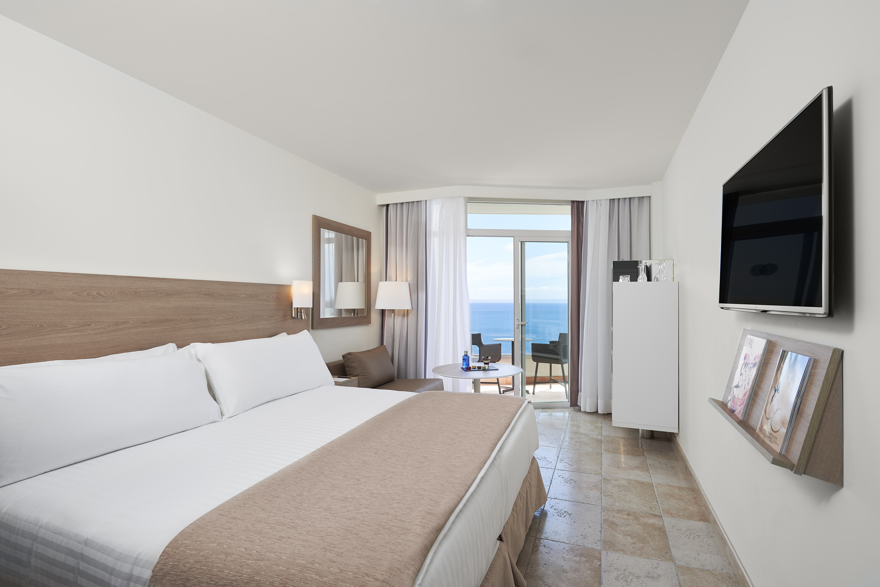 Modern hotel room with ocean view balcony, king bed, and flat-screen TV.