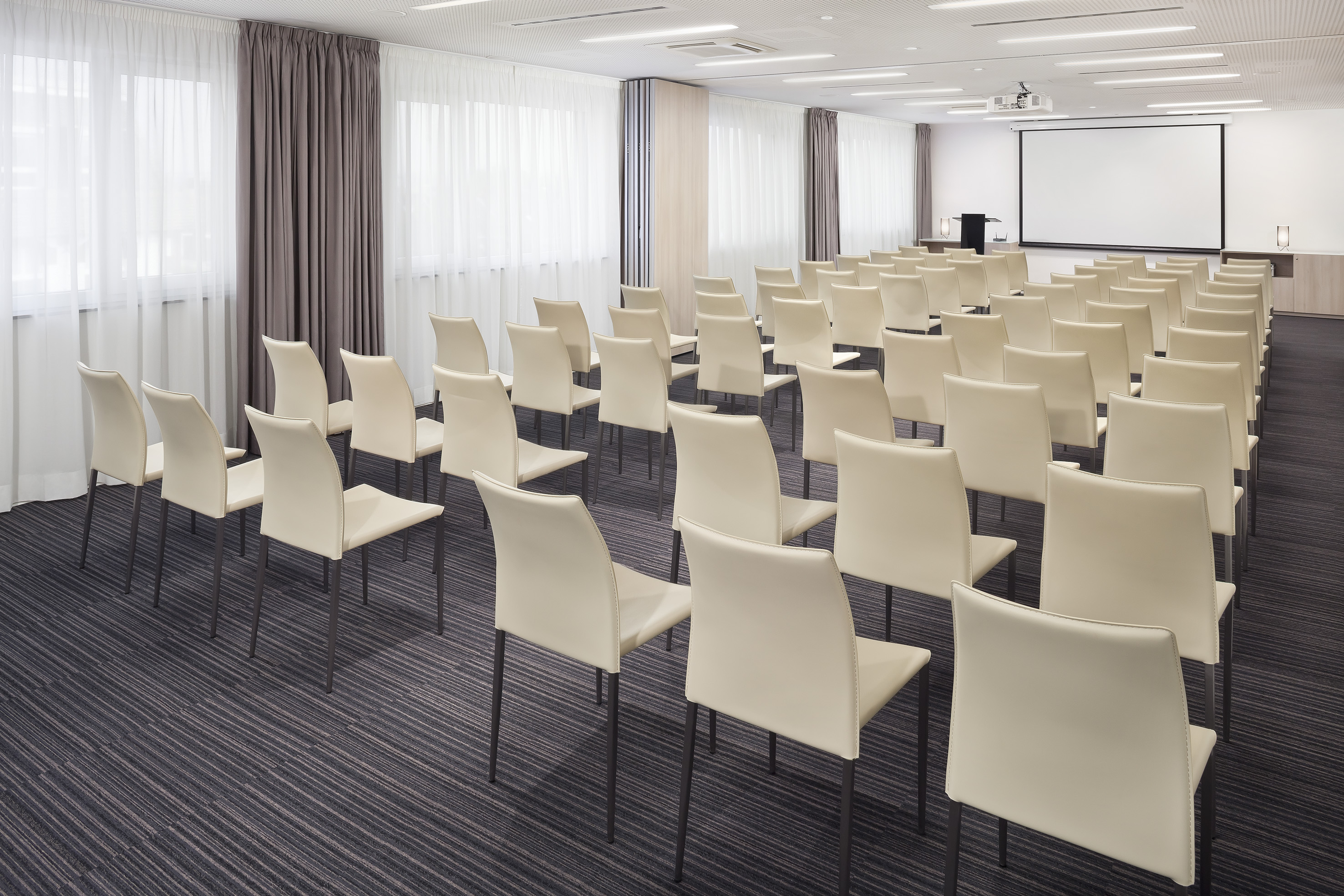 Empty conference room with cream chairs, projector screen, and windows.
