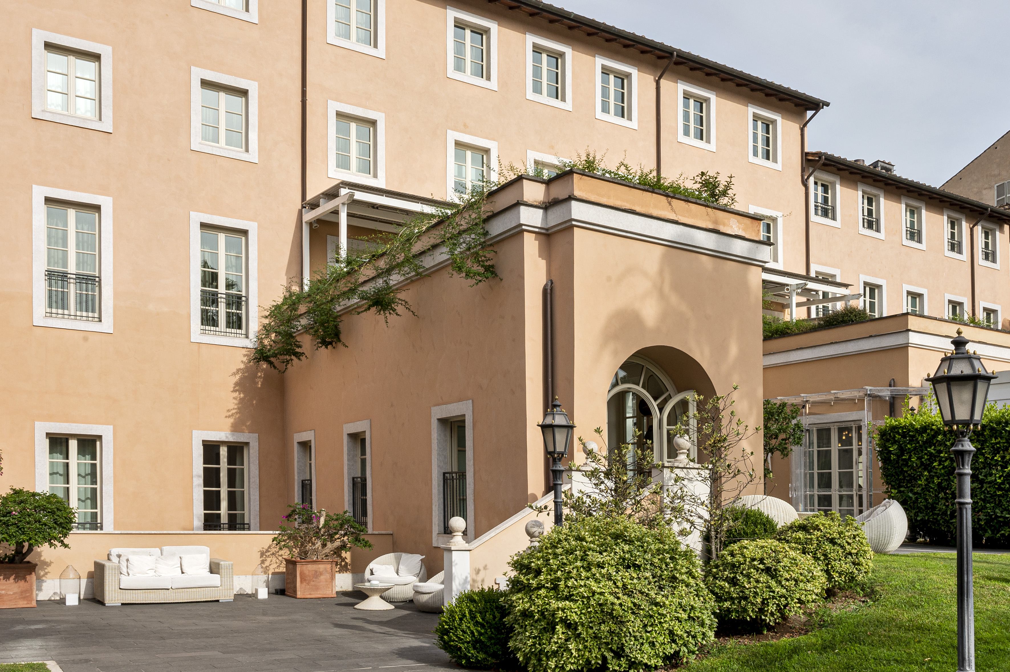 Peach building facade with terraces, outdoor patio seating, and garden.
