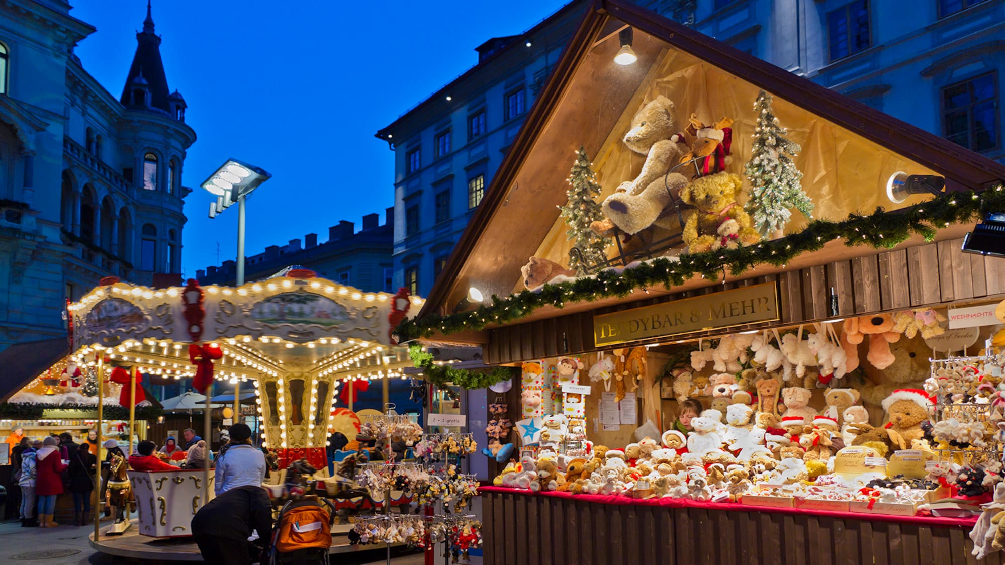 a group of people standing next to a booth with a carousel and a teddy bear