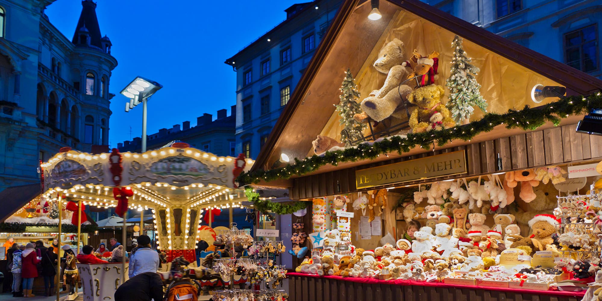 A group of people stands next to a booth featuring a carousel and a teddy bear.