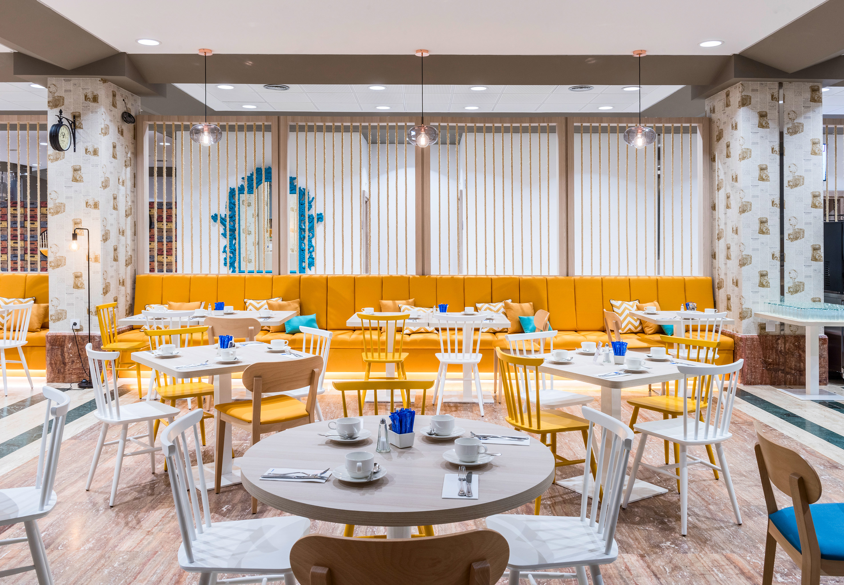 Vibrant hotel dining room with yellow banquette seating and white tables.