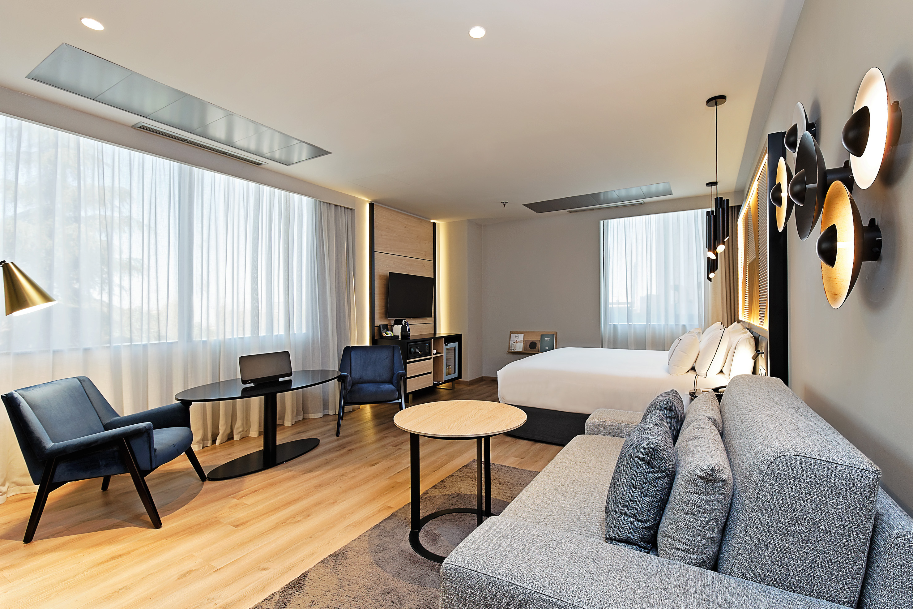 Contemporary hotel guest room featuring a bed, sofa, desk, and large windows.