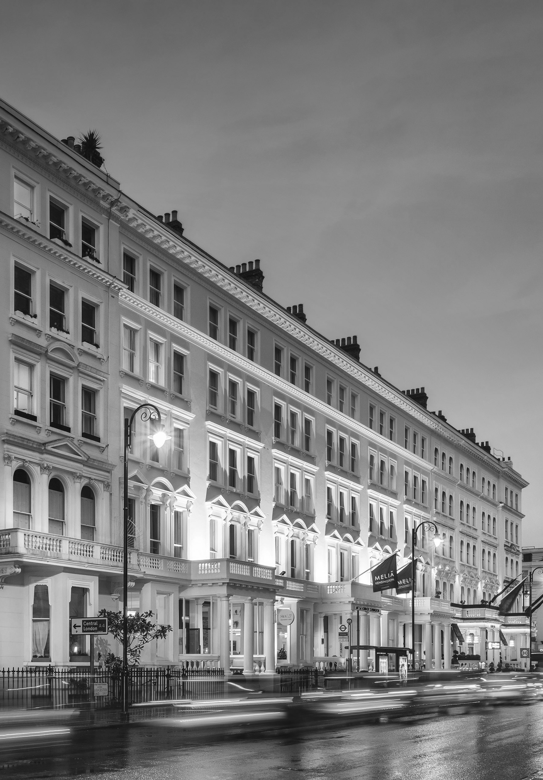 Black and white long exposure of Melia Kensington hotel in London at night with car light trails.
