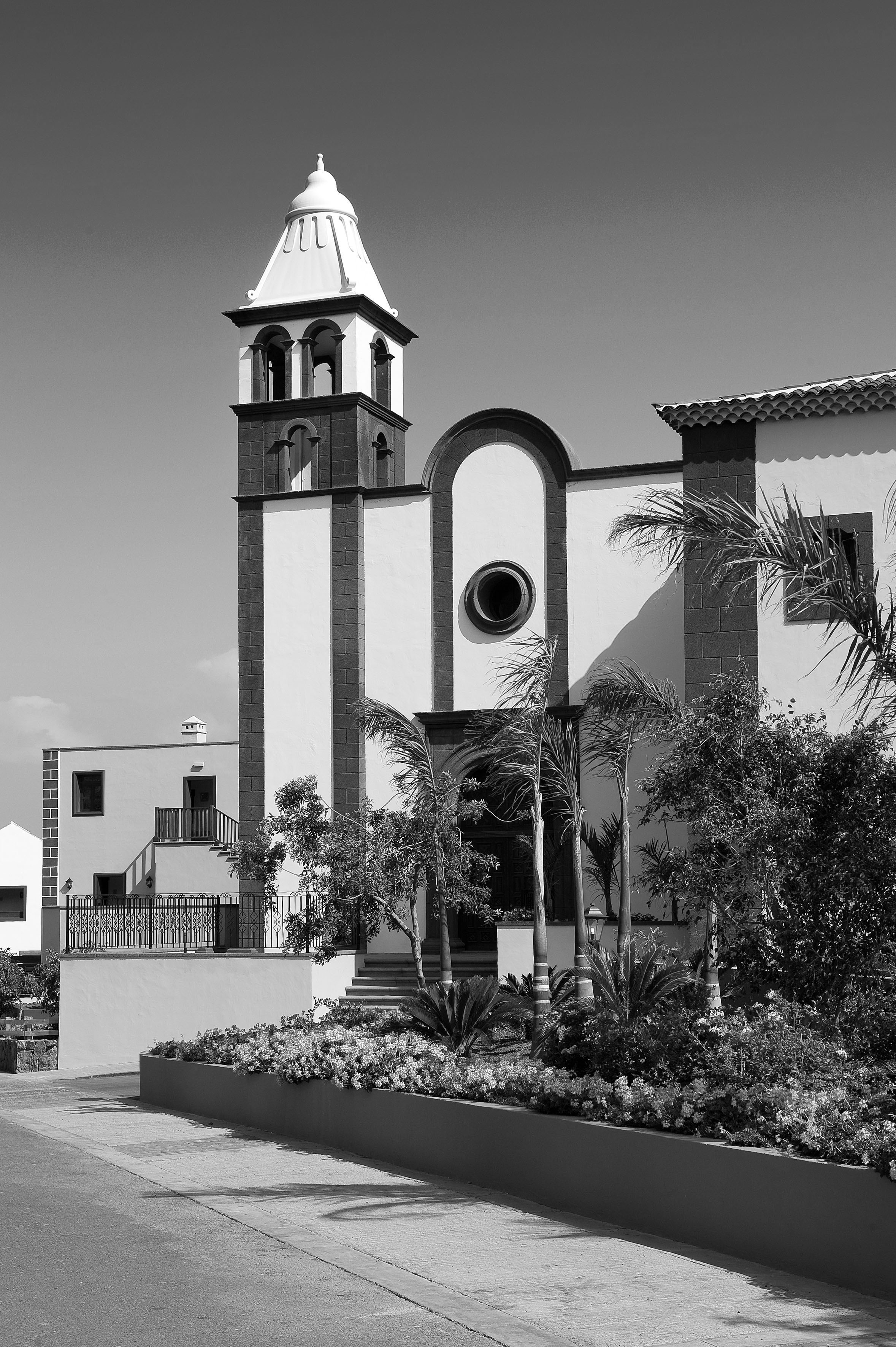 Black and white Spanish church bell tower, lush palms, and garden.