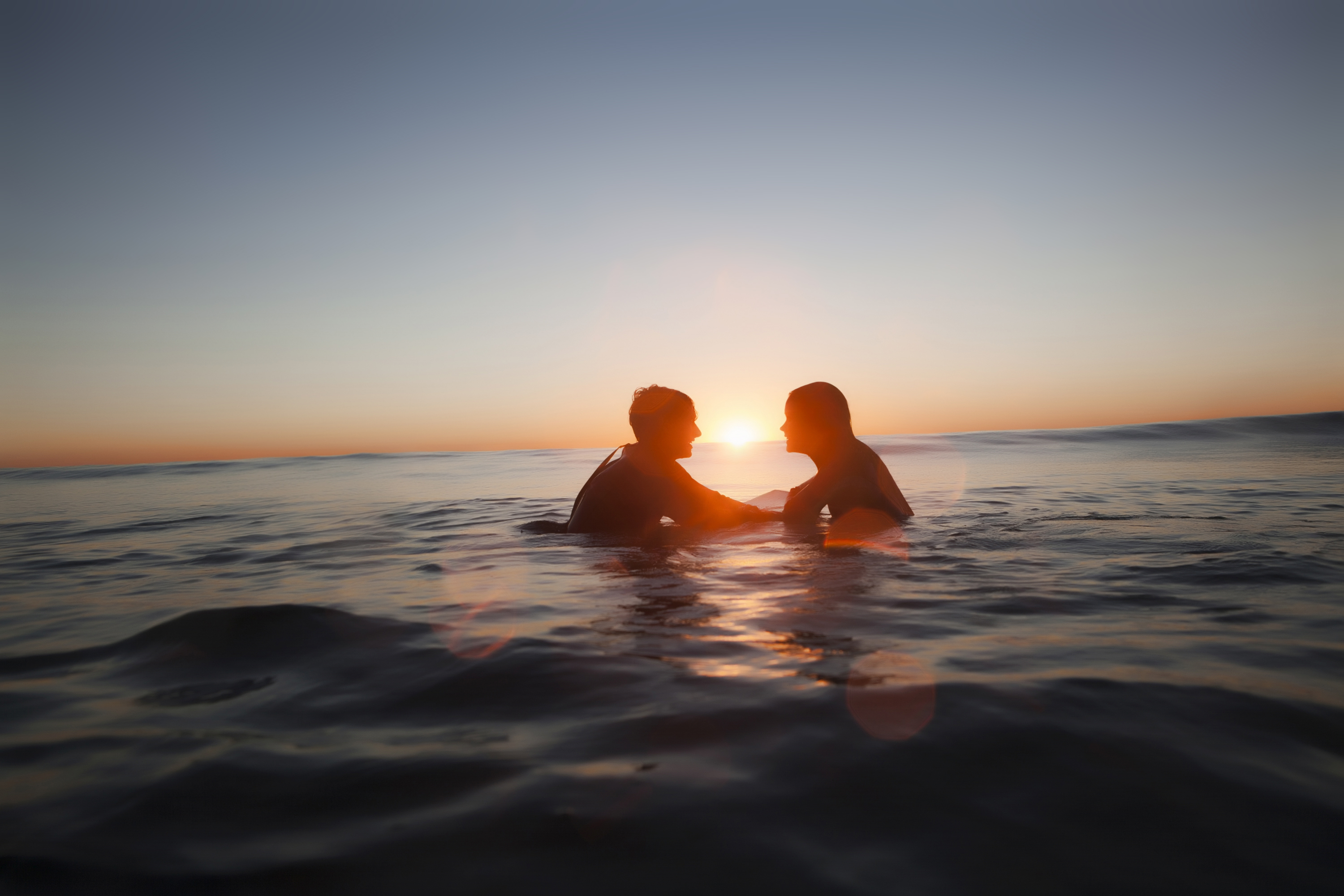 Siluetas de pareja en el mar al atardecer, sol en el horizonte.