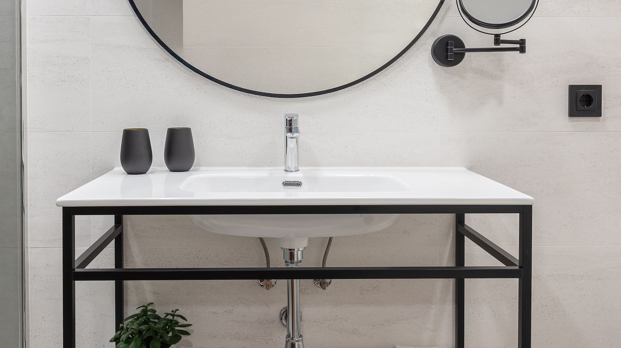 Modern bathroom with black round mirror, white vanity, and geometric floor tiles.