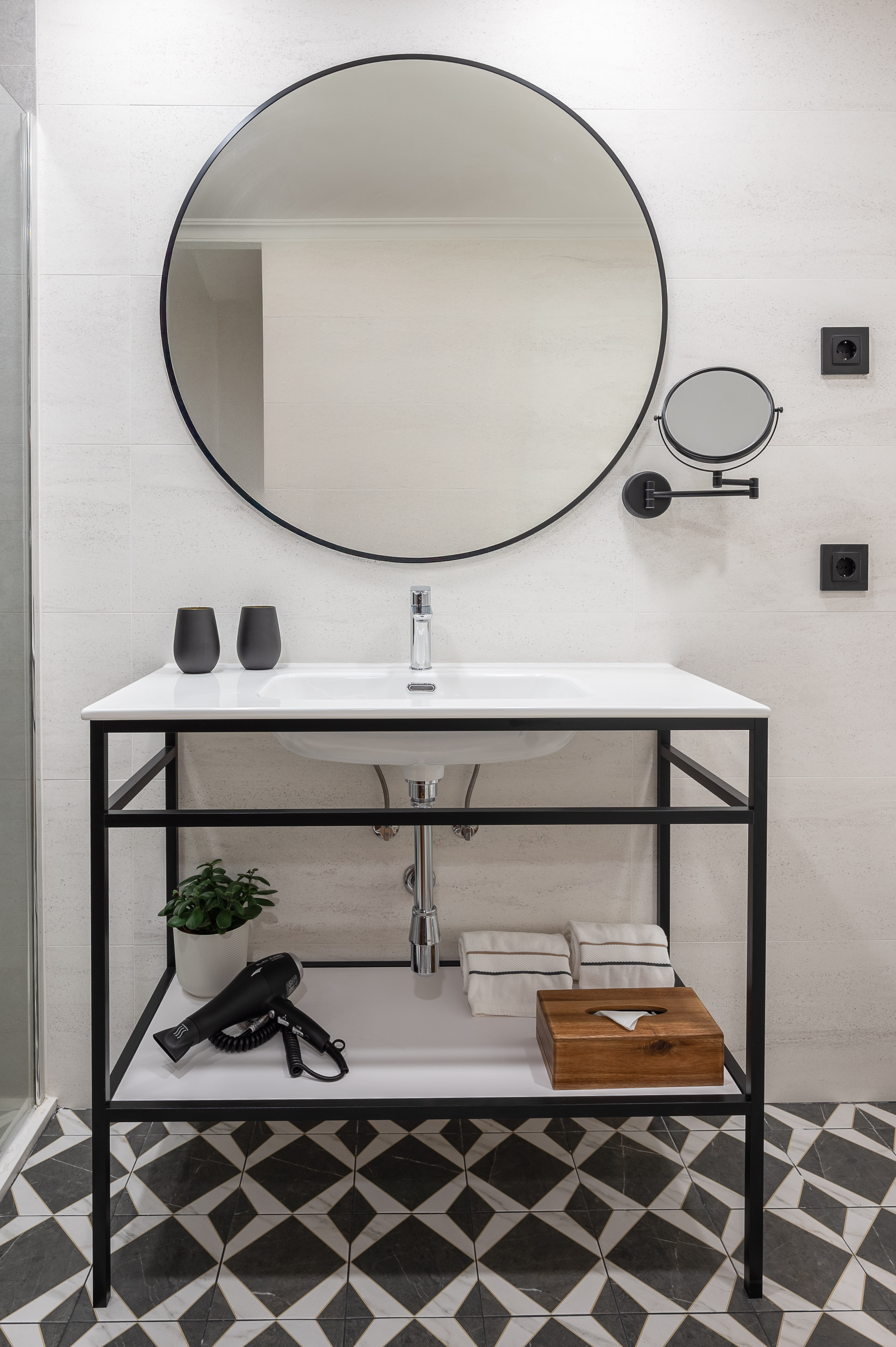 Modern bathroom with black round mirror, white vanity, and geometric floor tiles.