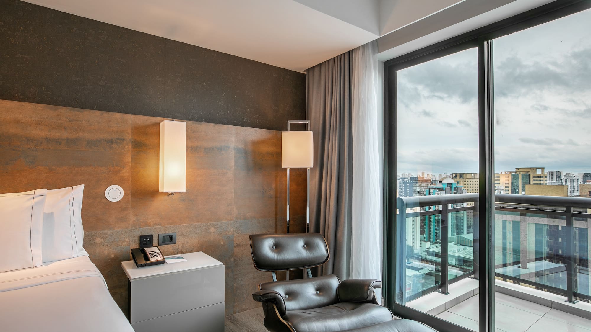 Quarto de hotel moderno com cama, poltrona de couro e vista para a cidade. - Grand Premium com Varanda - Meliá Ibirapuera, São Paulo