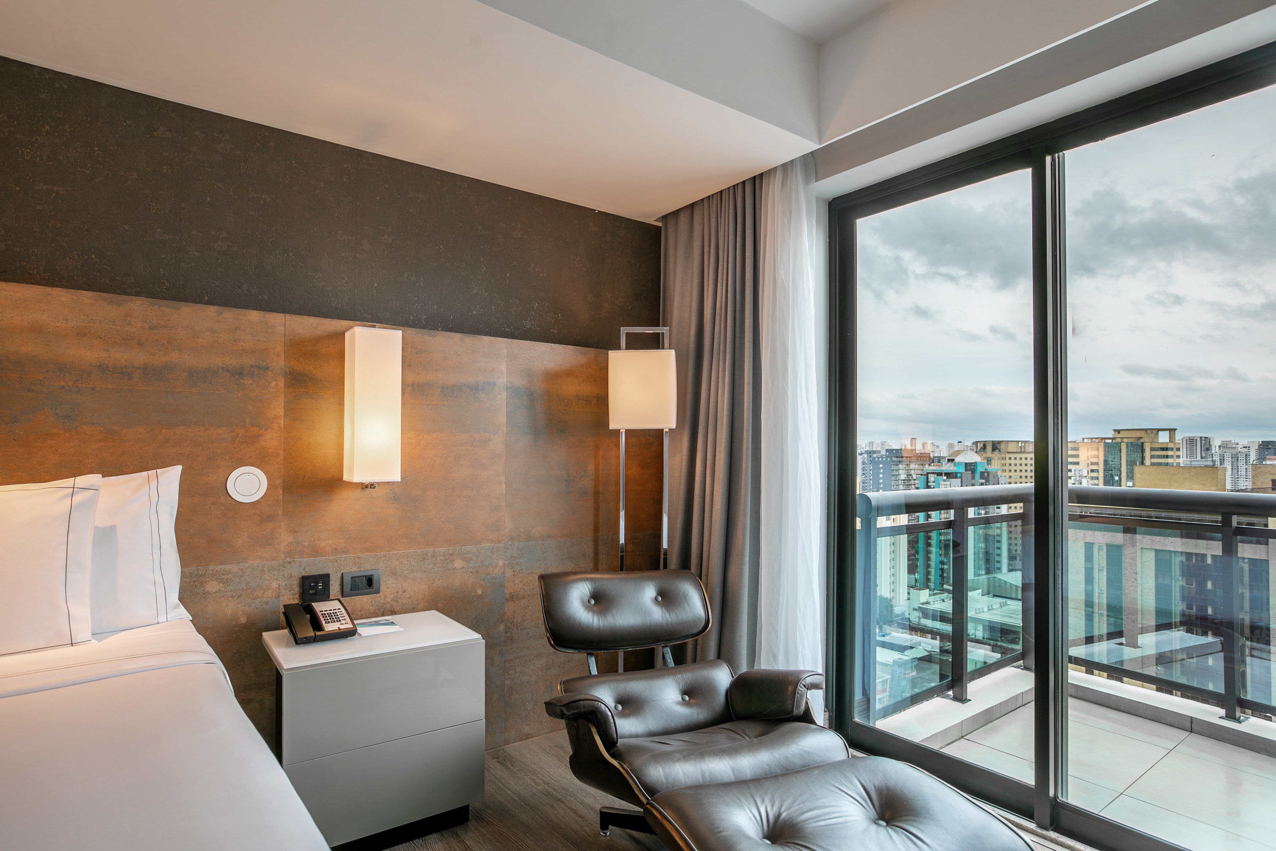 Quarto de hotel moderno com cama, poltrona de couro e vista para a cidade. - Grand Premium com Varanda - Meliá Ibirapuera, São Paulo