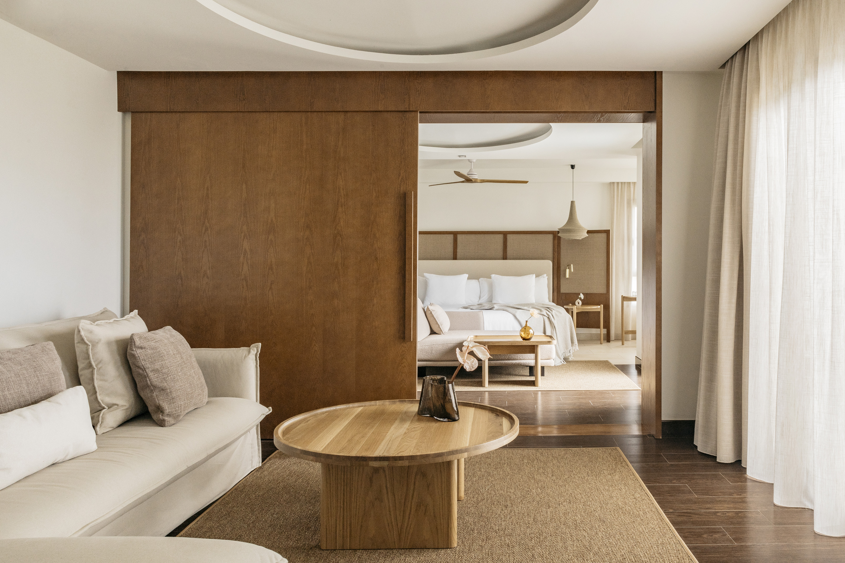 Modern hotel suite with living room, wood sliding door to bedroom.