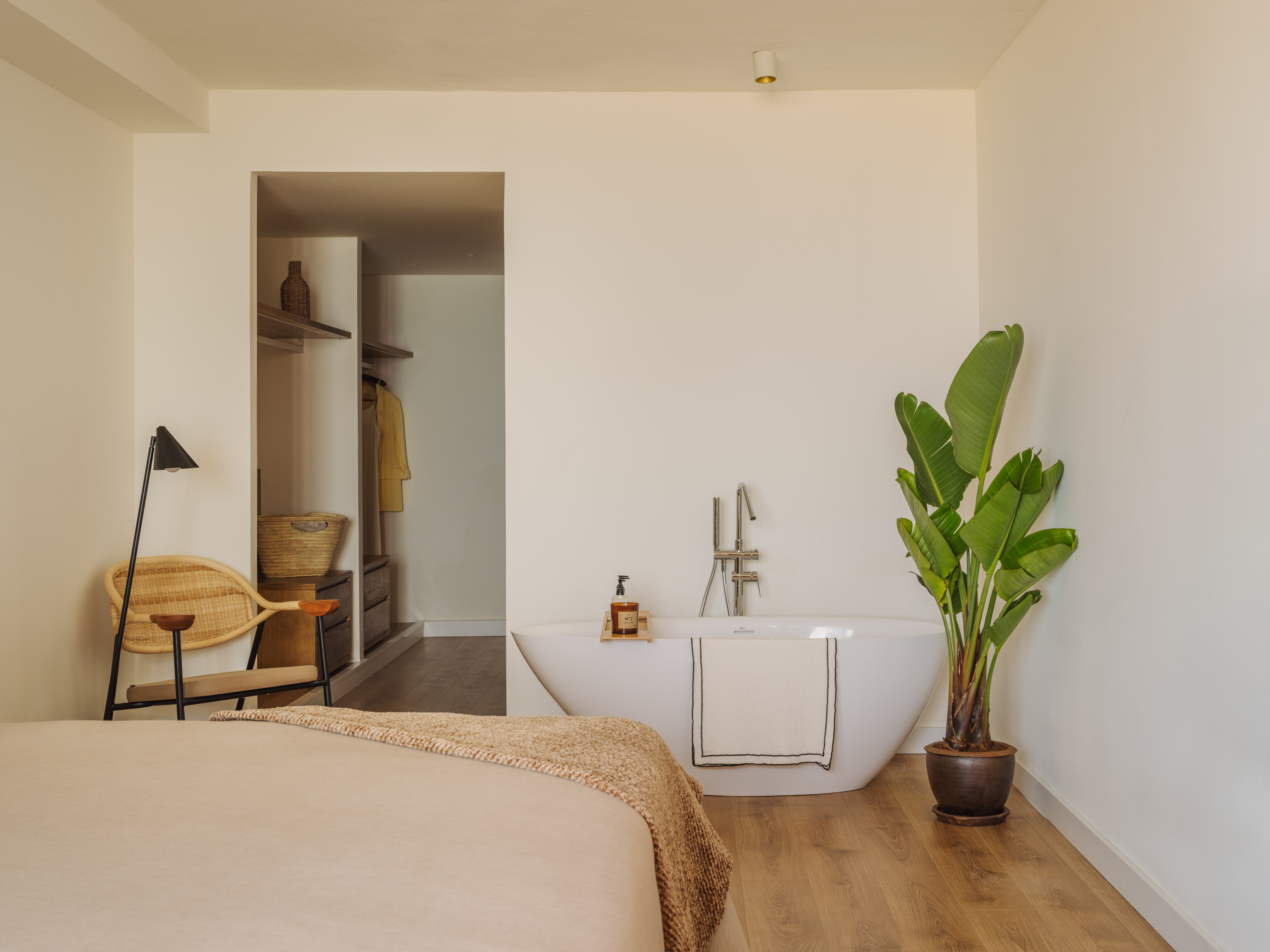 Modern bedroom with open bathroom, freestanding tub, and tropical plant.