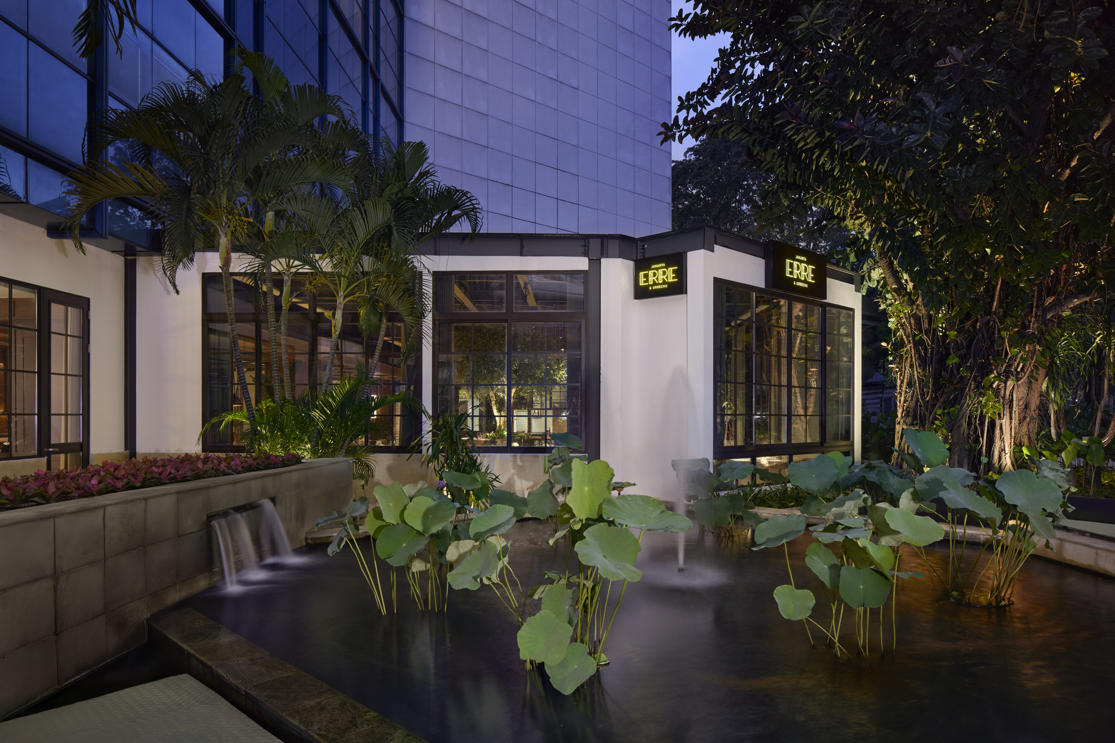 ERRE restaurant building exterior with pond, lotus, waterfall at night.