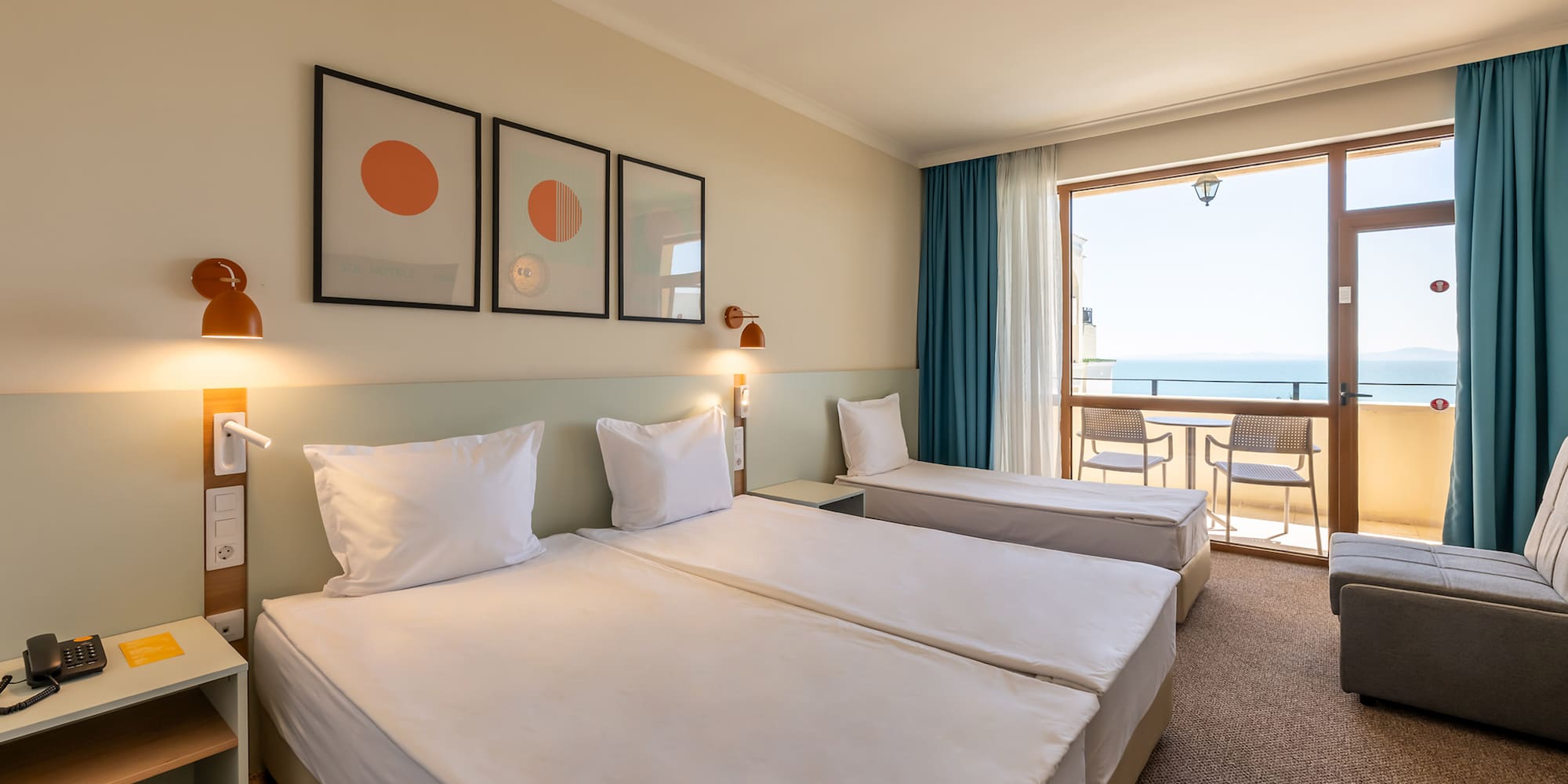 Bright hotel room with two beds, sofa, and balcony offering a sea view.