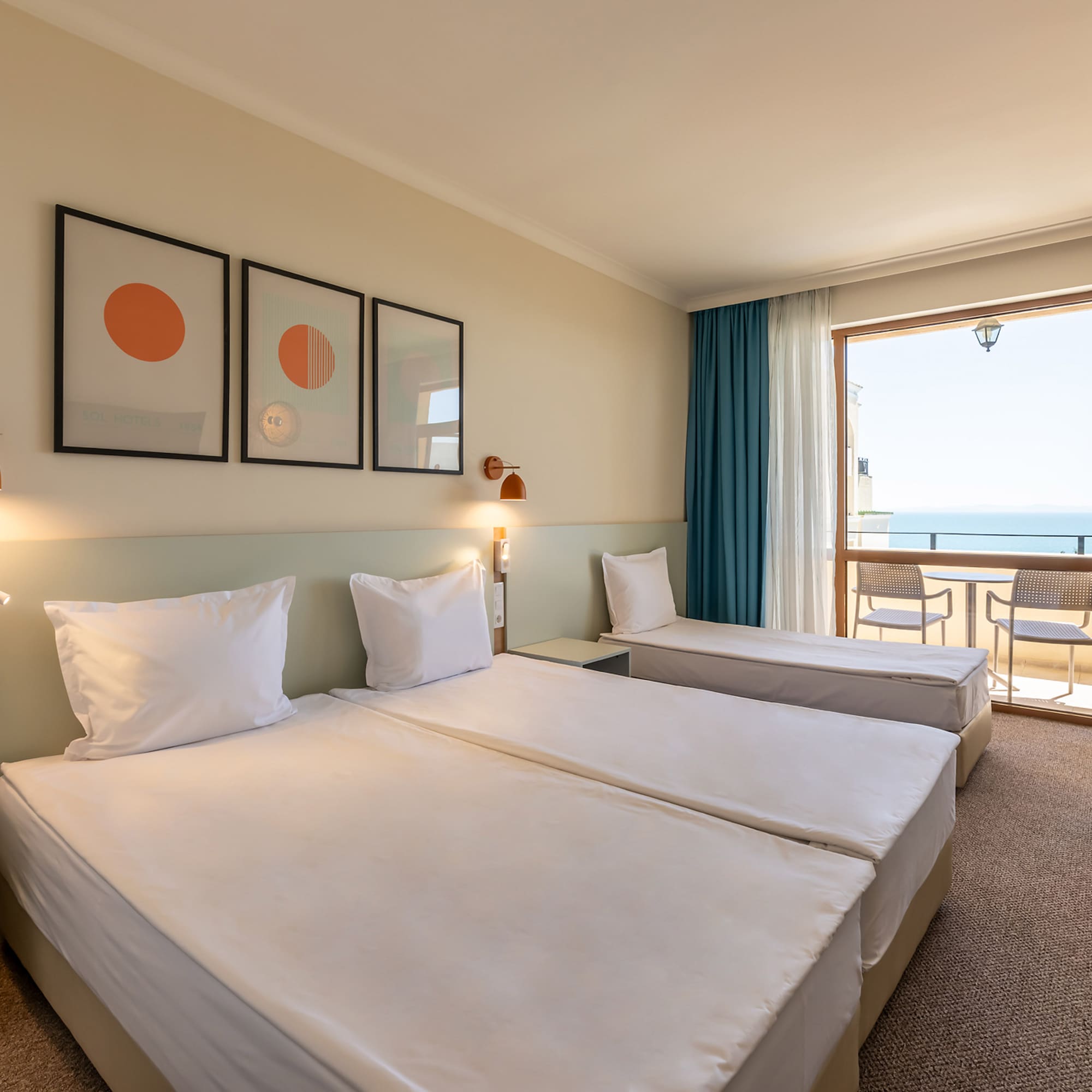 Bright hotel room with two beds, sofa, and balcony offering a sea view.