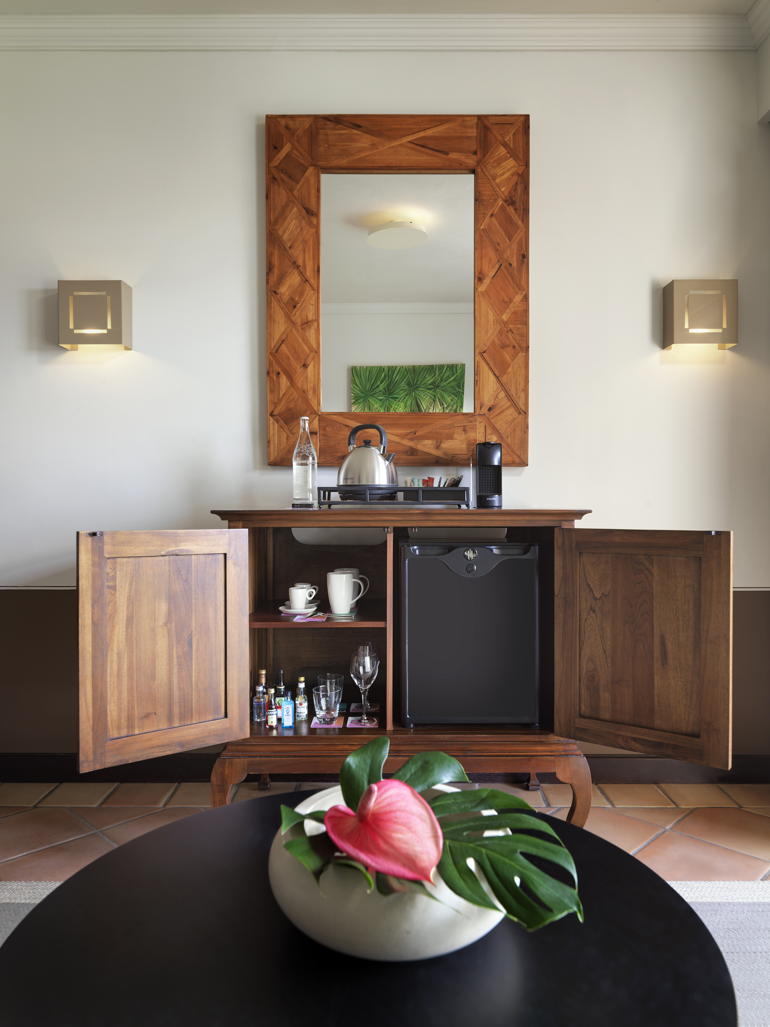 Wooden hotel minibar cabinet with mini-fridge, coffee, tea, drinks, and mirror.