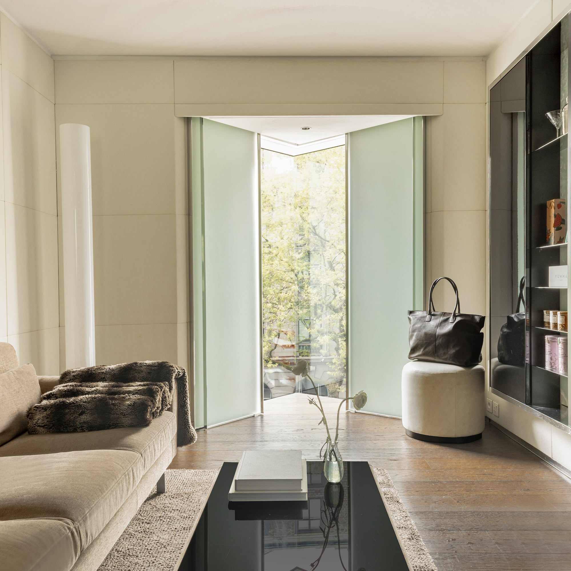Modern living room with beige sofa, frosted glass pivot doors, and wood floor.