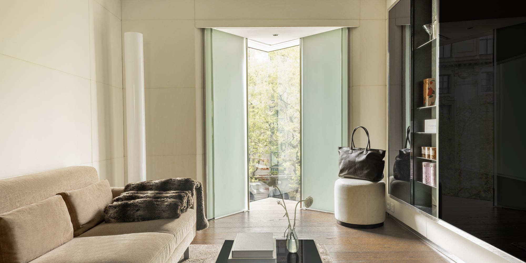 Modern living room with beige sofa, frosted glass pivot doors, and wood floor.