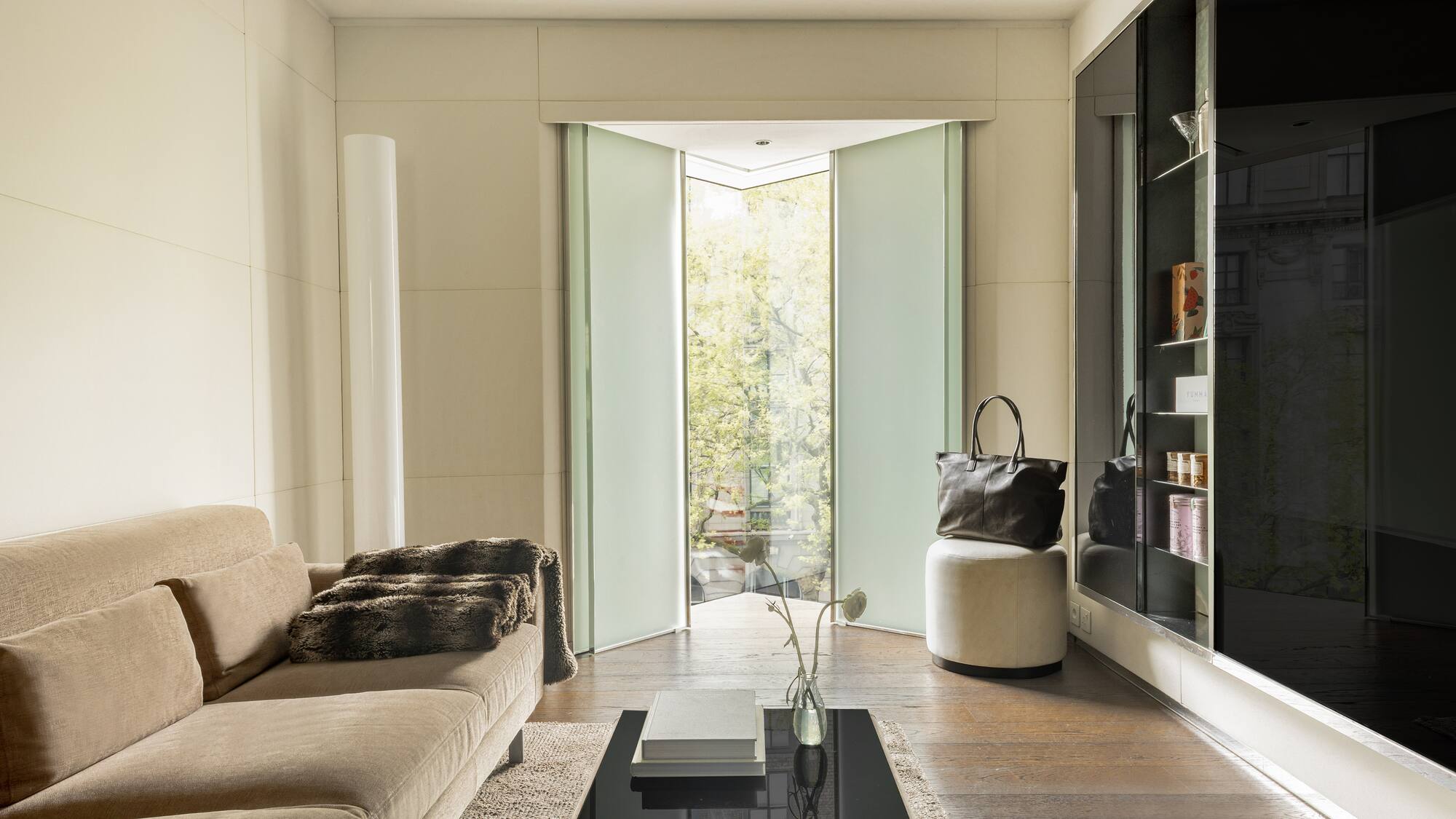 Modern living room with beige sofa, frosted glass pivot doors, and wood floor.