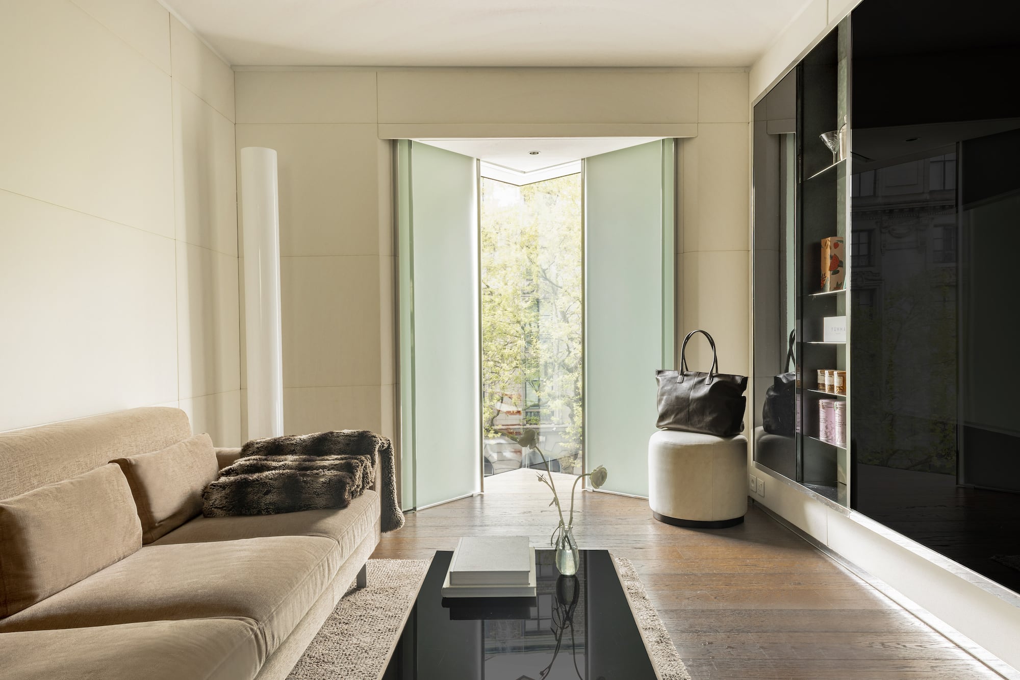 Modern living room with beige sofa, frosted glass pivot doors, and wood floor.