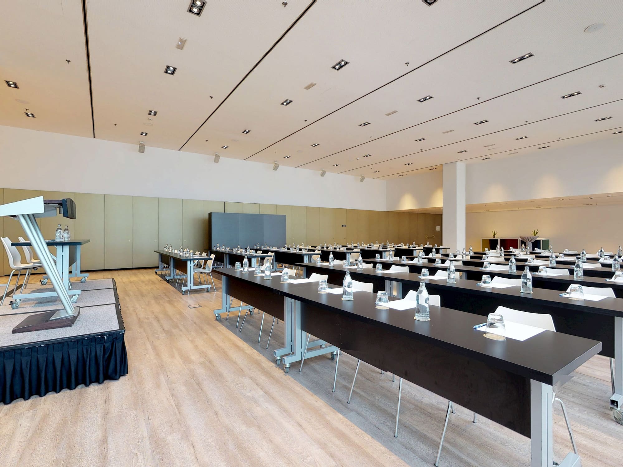 Sala de conferencias moderna con atril, pantalla y mesas para reuniones.