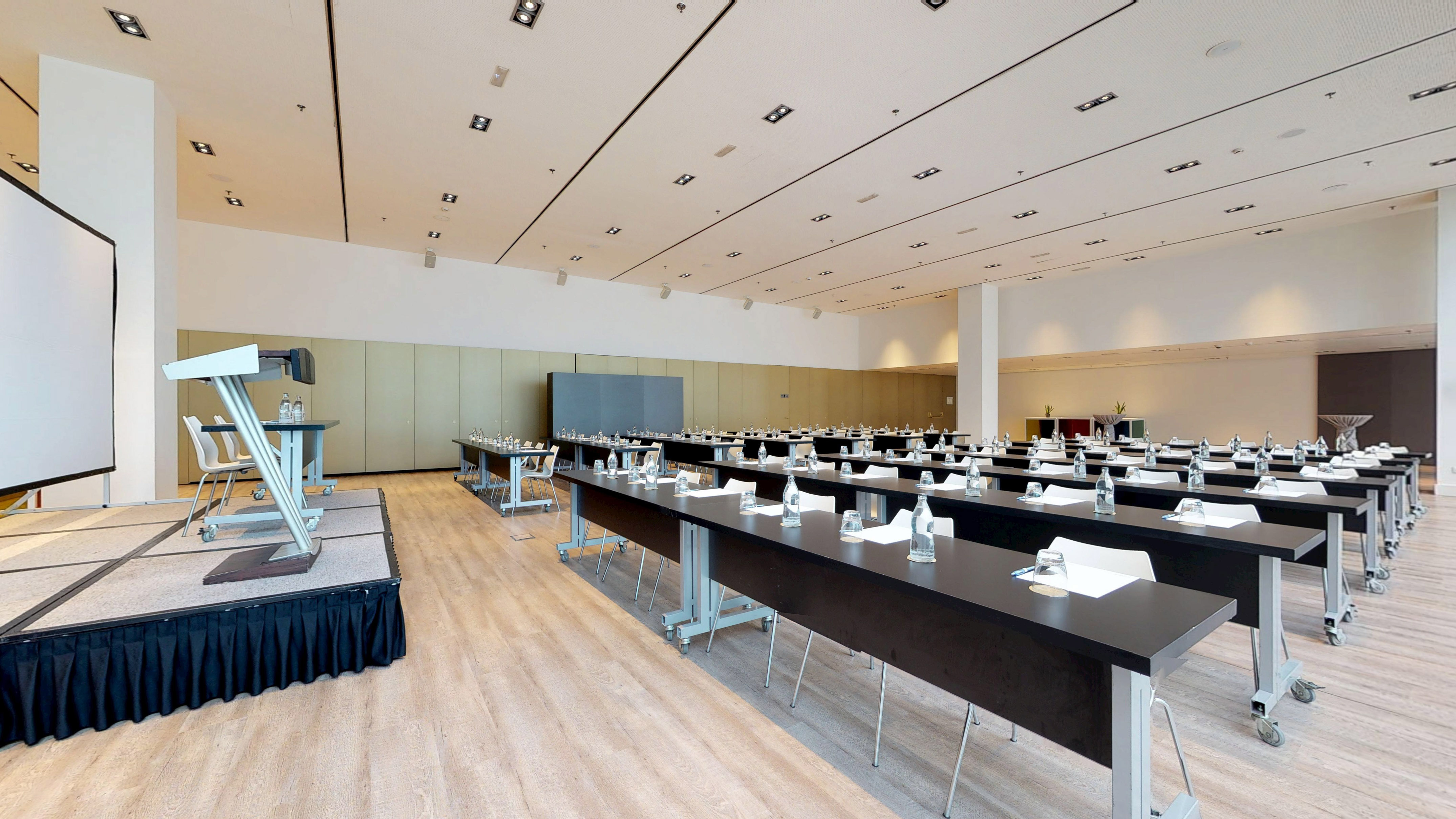 Sala de conferencias moderna con atril, pantalla y mesas para reuniones.