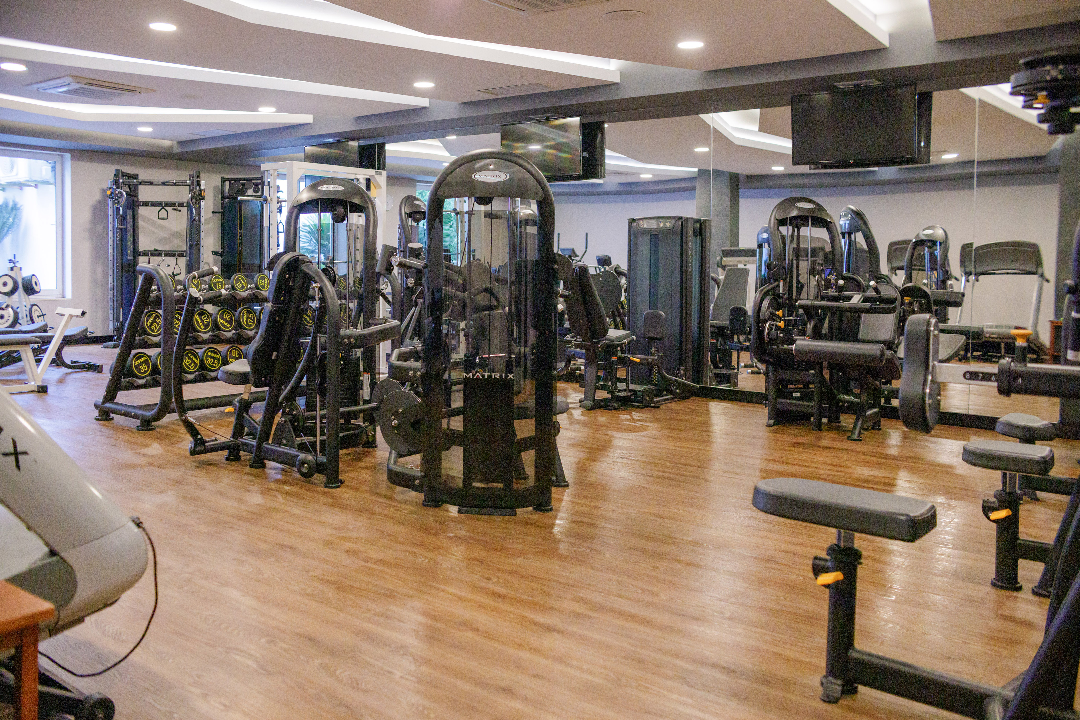Modern gym with Matrix exercise machines, dumbbell rack, and mirrored walls.