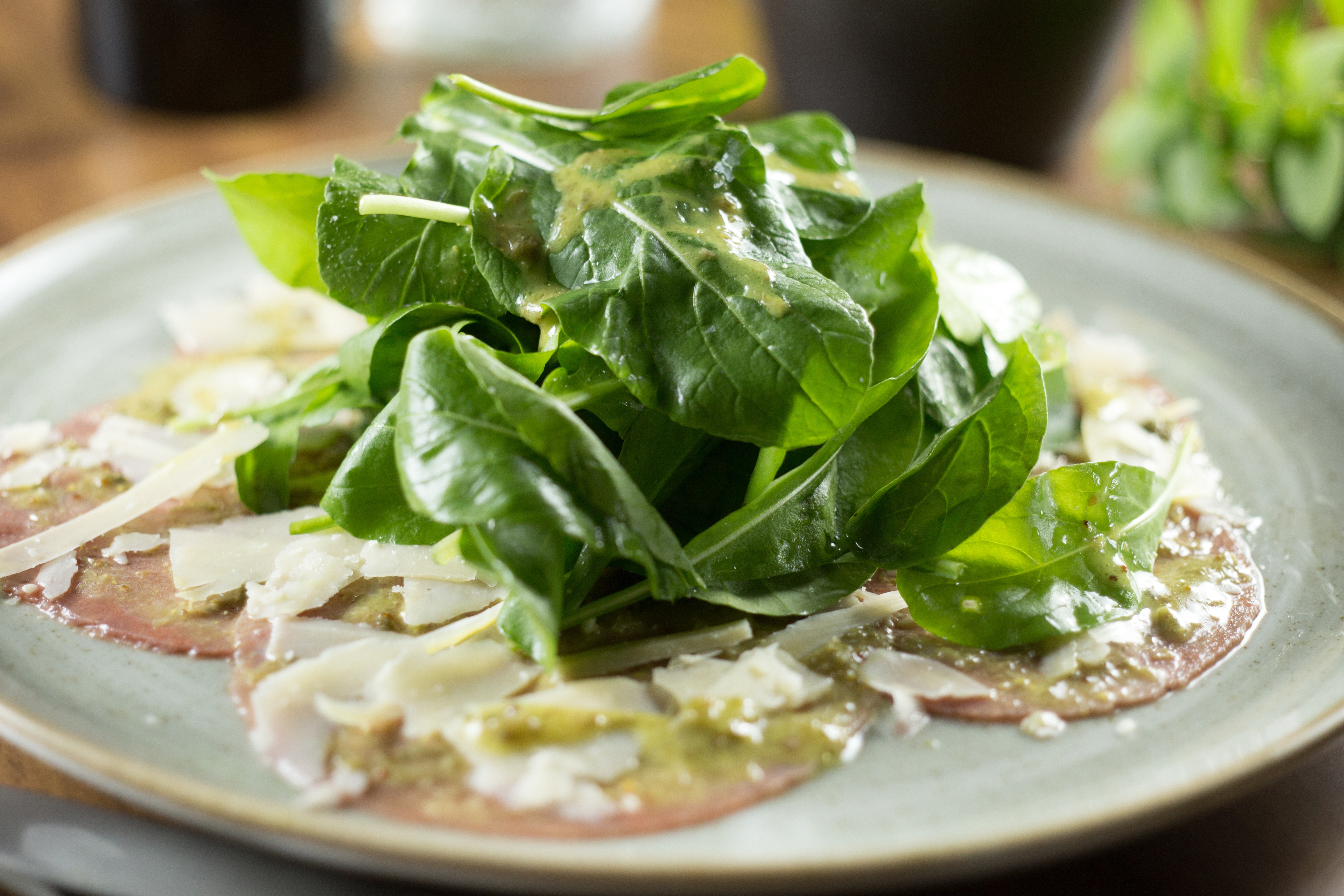 Beef carpaccio with fresh arugula, shaved Parmesan, and pesto.