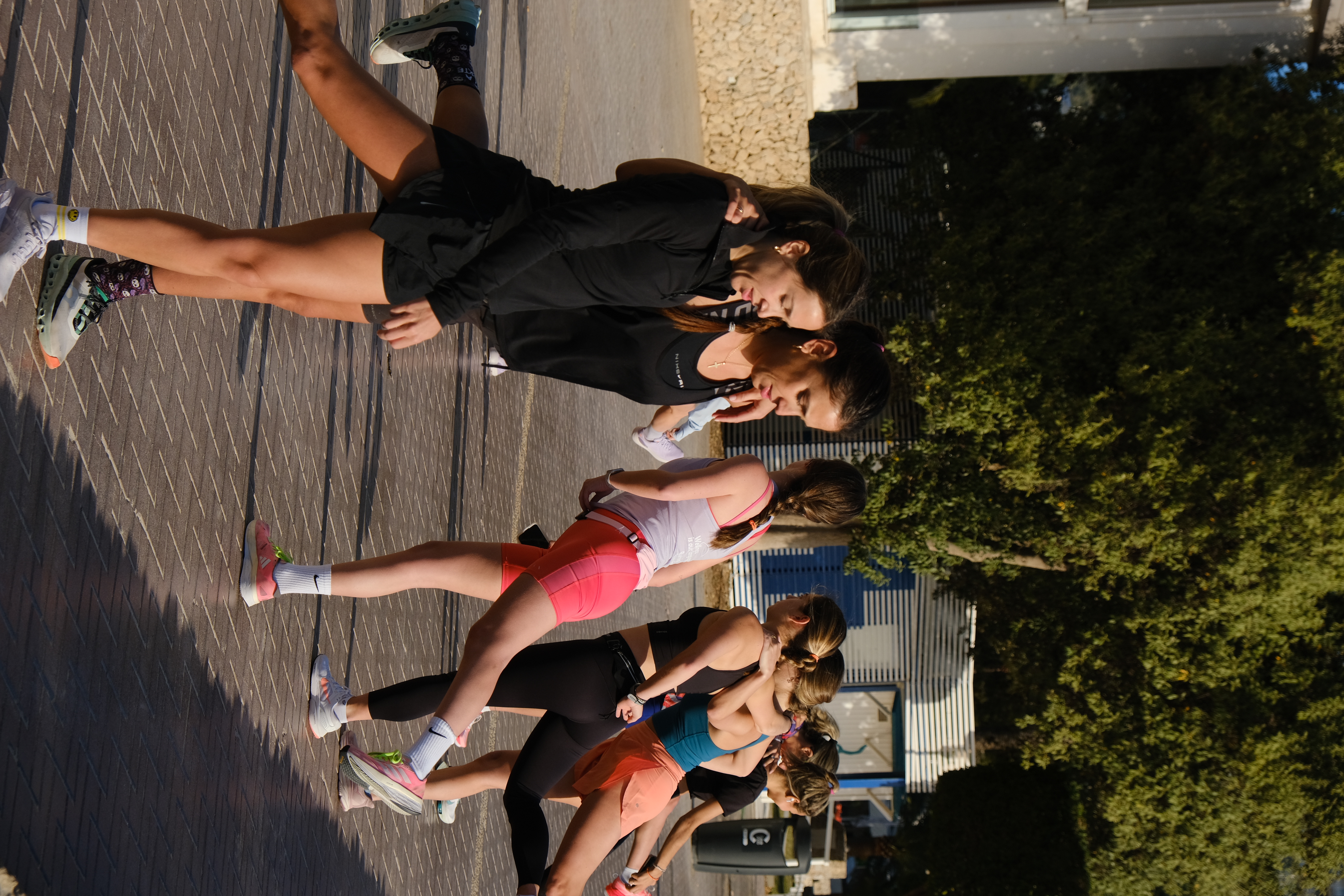 Women's fitness group stretching legs outdoors in athletic workout gear.